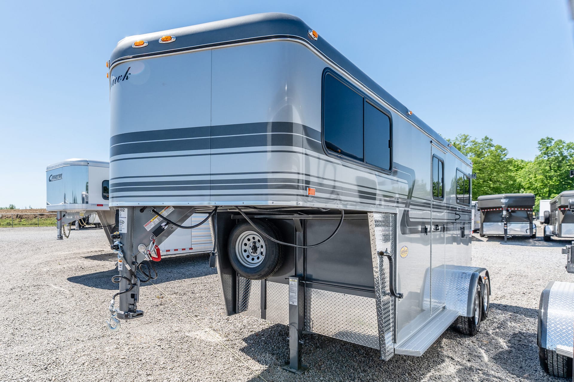 Large blue-and-gray fifth-wheel RV trailer parked on a gravel lot with other trailers in the background