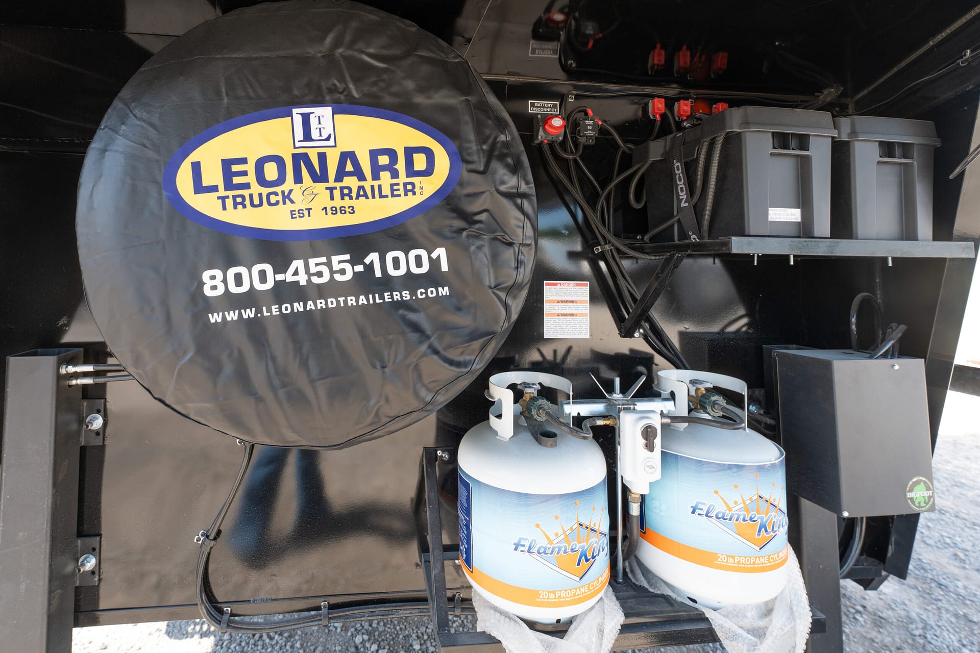 Spare tire cover with Leonard Truck & Trailer logo mounted inside a trailer along with propane cylinders and battery components nearby.