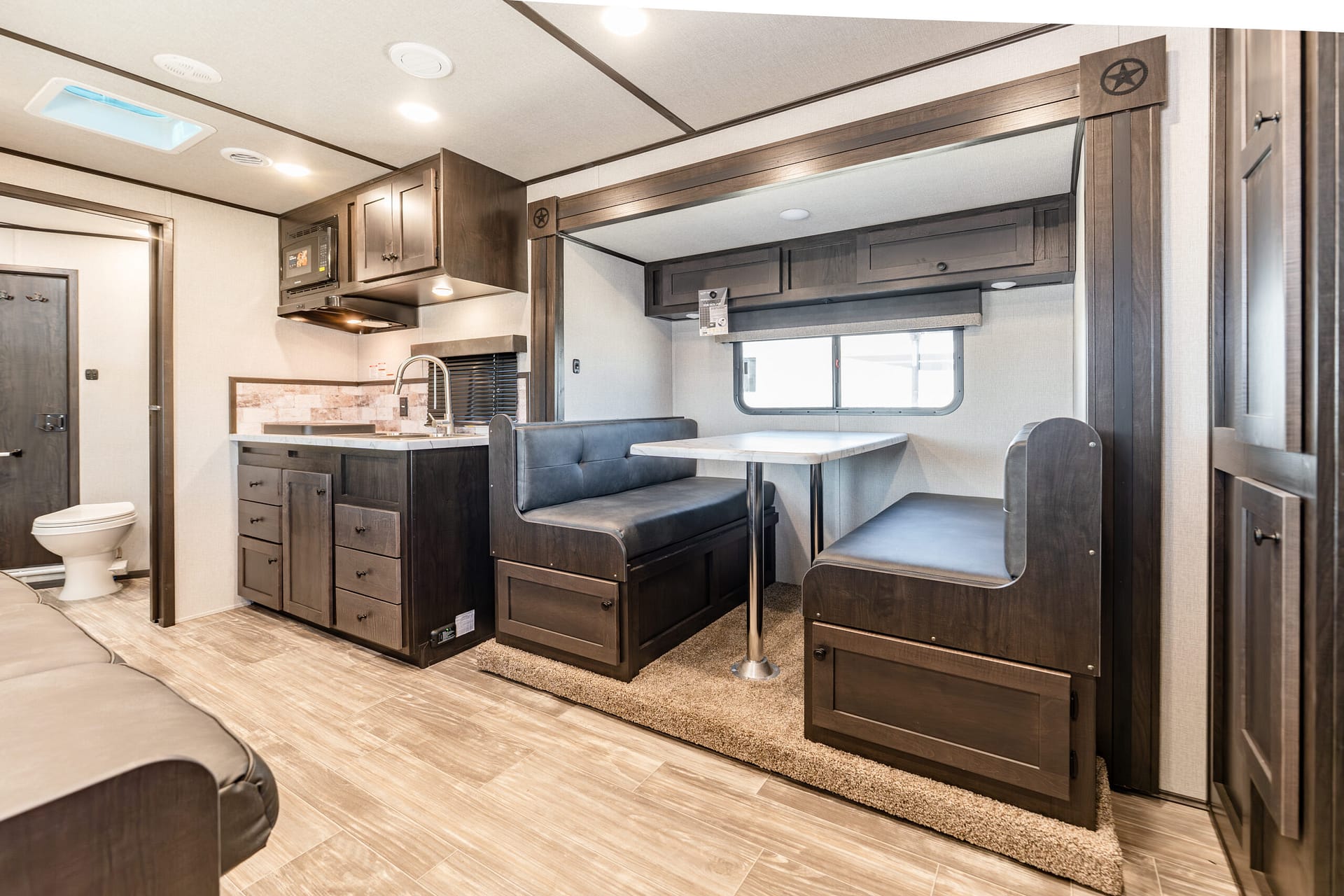 Interior of a modern RV with dark wood cabinets, dinette booth, and compact kitchenette