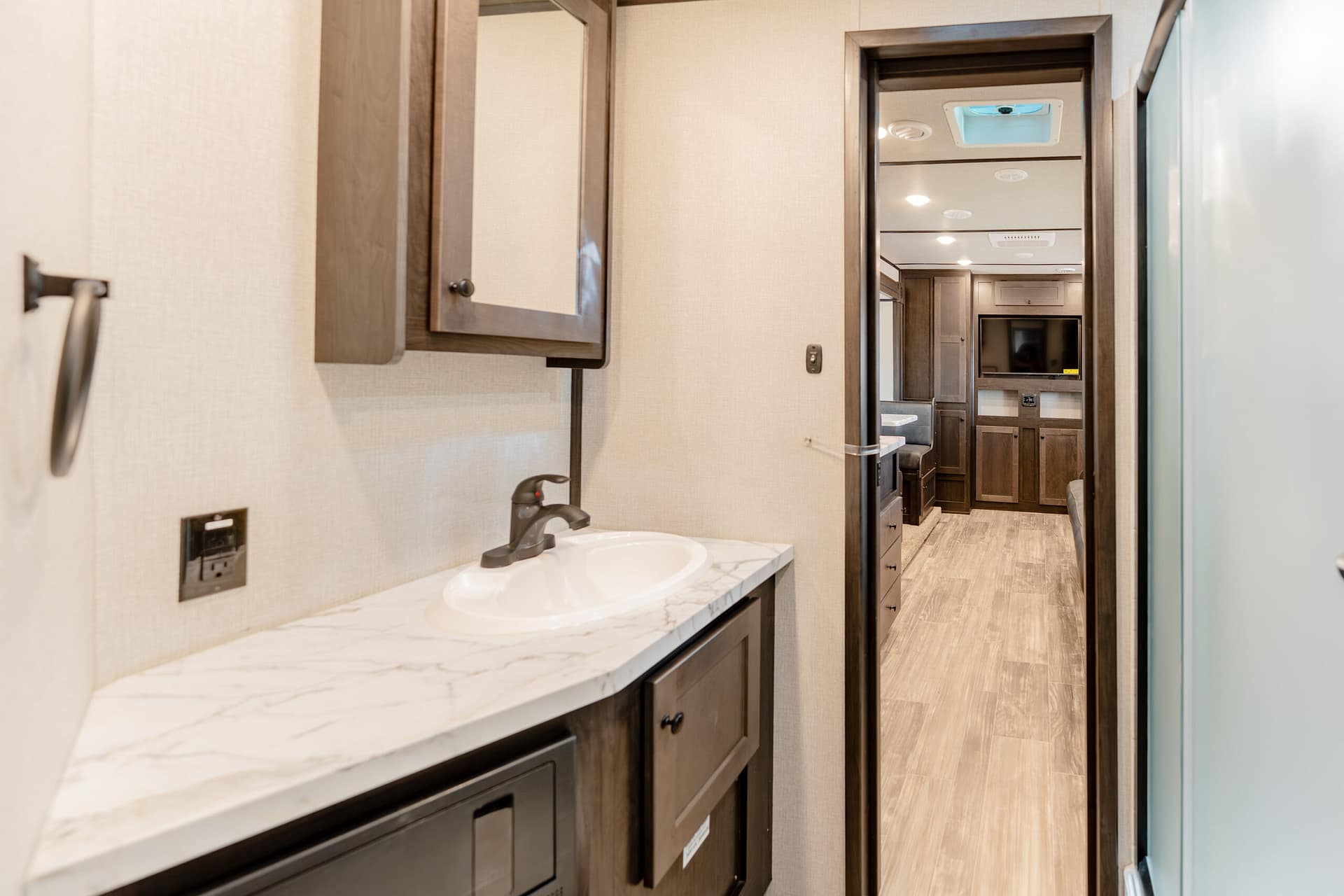 RV bathroom vanity with marble countertop, dark wood cabinets, and medicine cabinet.