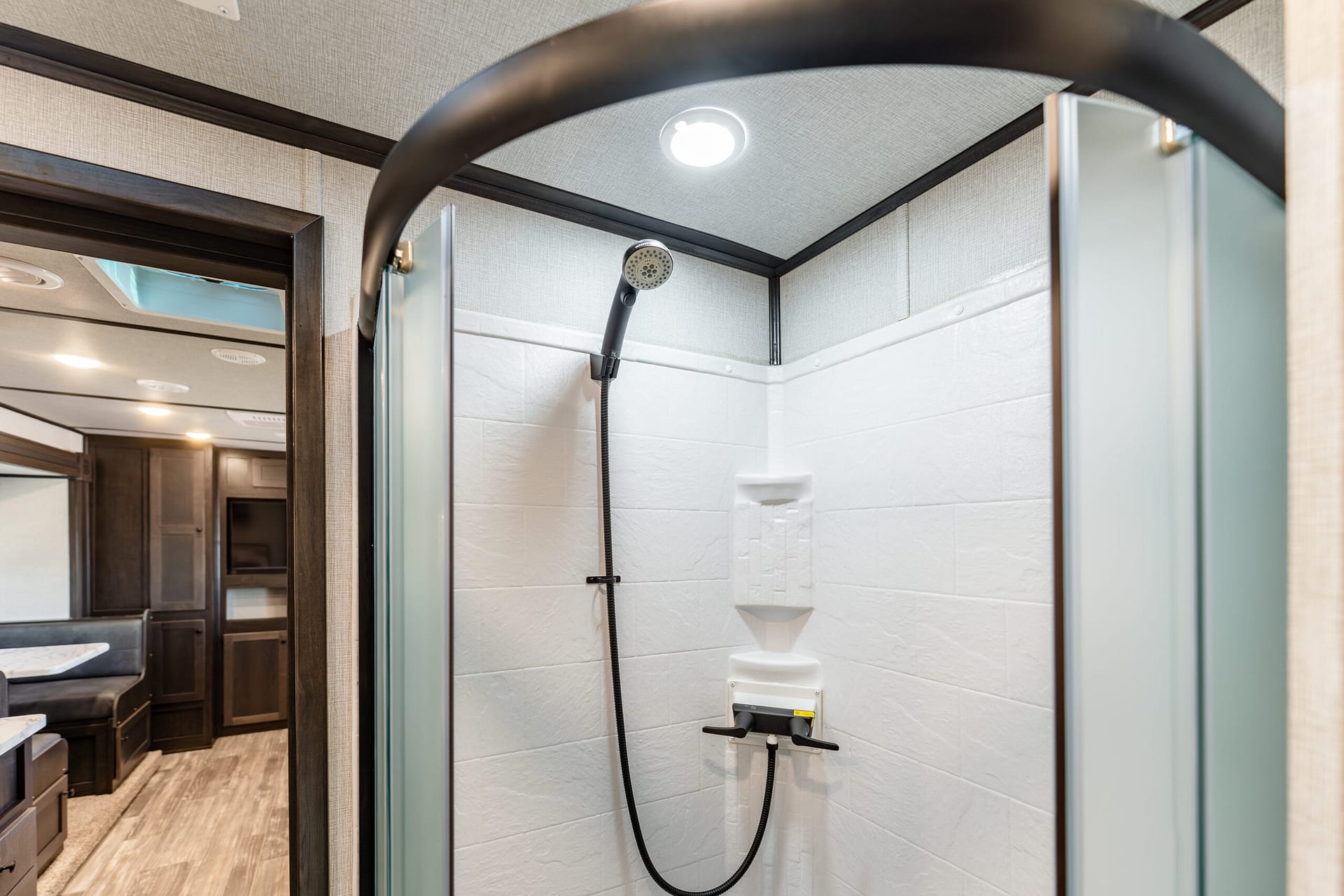 Shower stall with white tiled walls, handheld showerhead, and curved glass doors inside a bathroom area of a RV or small home.