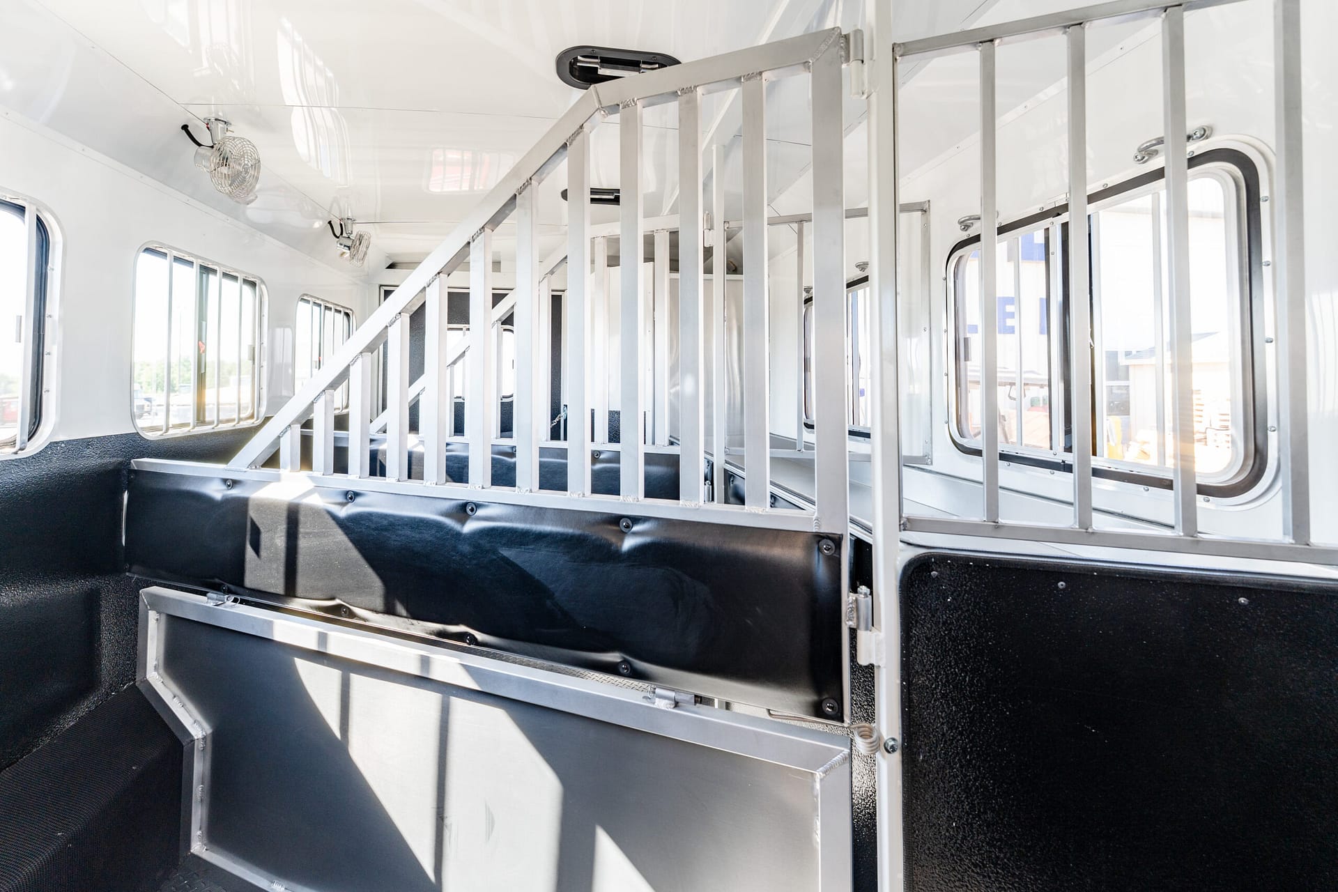 Interior of a vehicle with metal stall dividers and black cushioned floor, likely a livestock trailer or horse transport