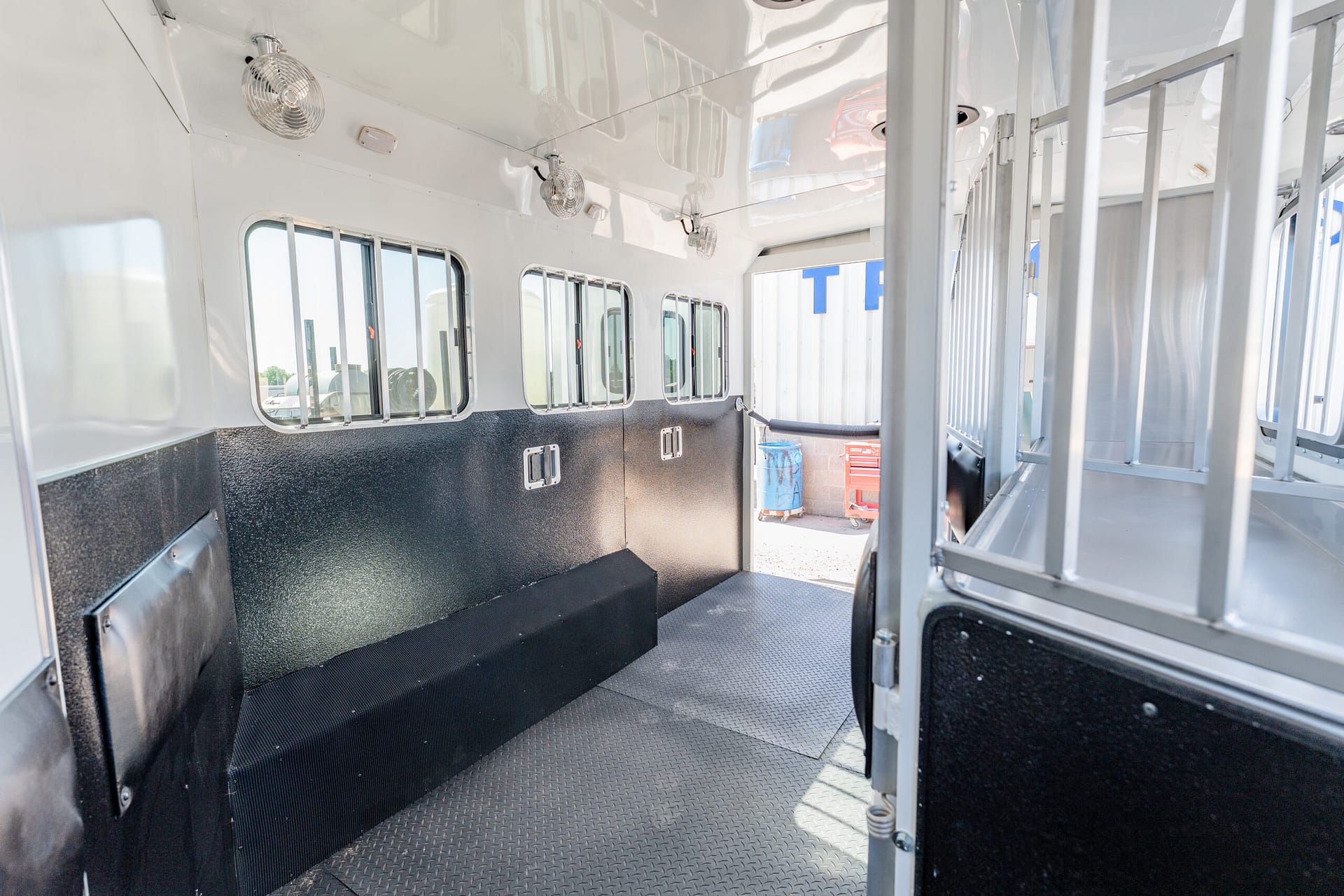 Interior of a white horse trailer with barred windows, textured black lower walls, and diamond-plate floor.
