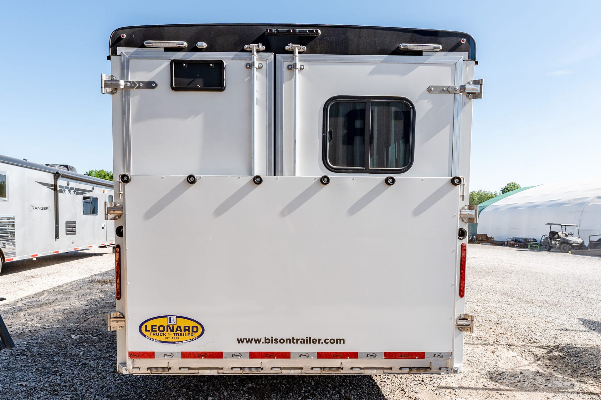 Rear view of a silver trailer with a small windowed door, metal latches, and red reflectors; Leonard Truck & Trailer logo visible at bottom.