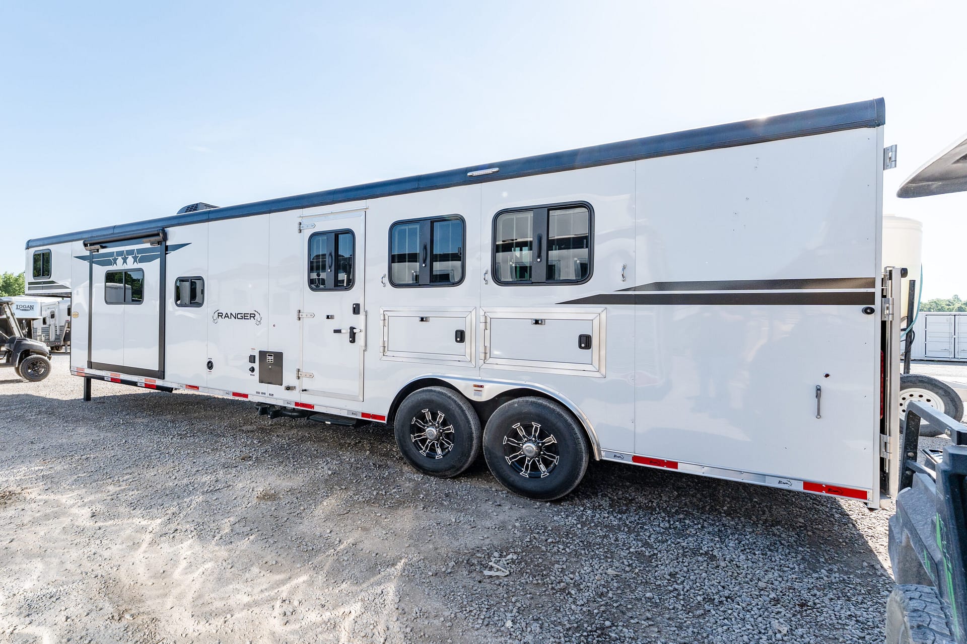 White RV trailer with multiple windows and a rugged dual-axle setup parked on gravel lot; Ranger branding visible on door area.