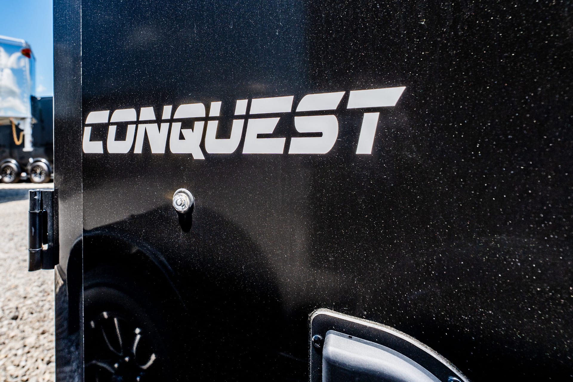 Close-up of a black metal surface with a white stylized logo reading 'LONQUEST' on a trailer.