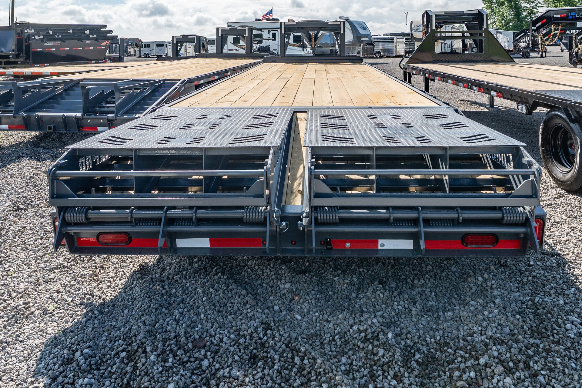 Wide view of empty flatbed trailers with wooden decks and metal ramps in a gravel lot core to a trailer lot setting.