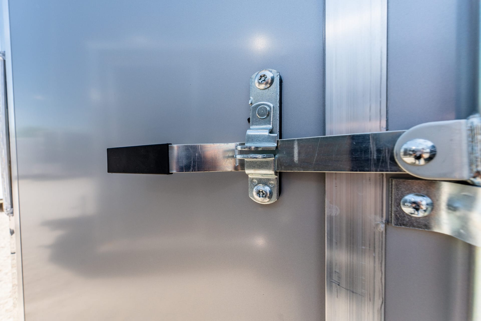 Close-up of a metal door latch and strike plate mounted on a gray industrial panel.