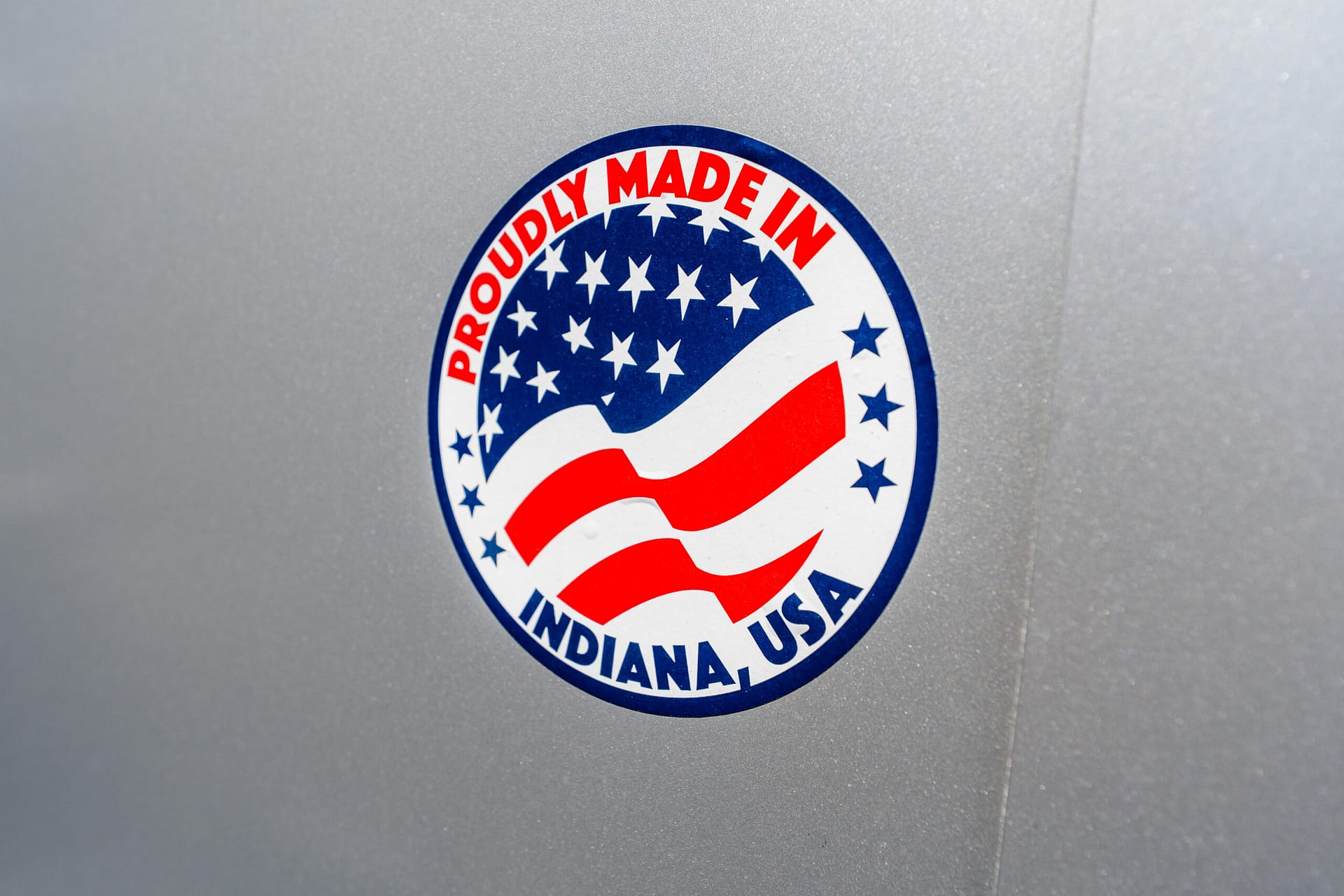 Circular sticker reading 'Proudly Made in Indiana, USA' with stars and stripes on a silver/metal surface.