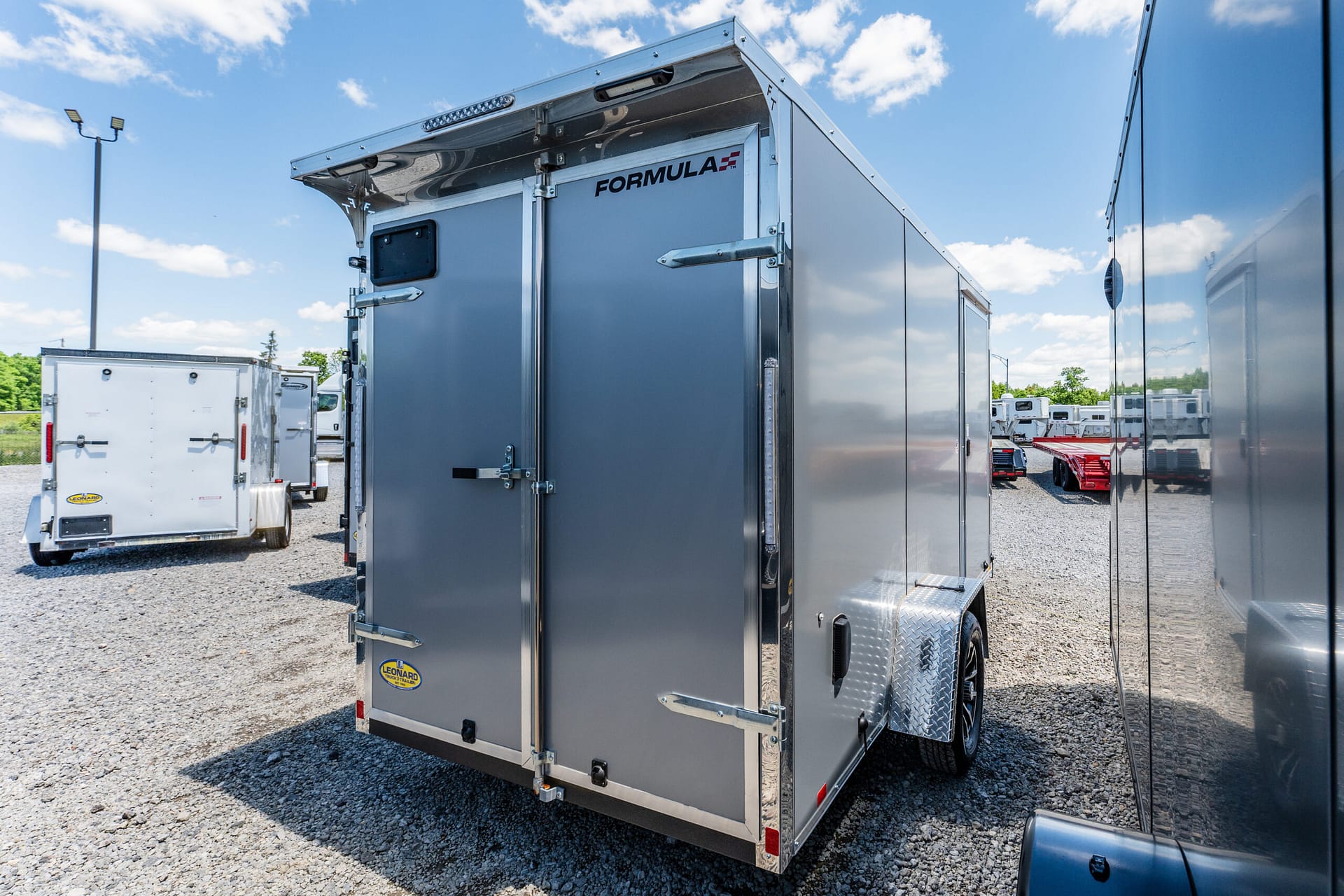 Large gray cargo trailer with 'FORMULA' branding in a truck yard, side doors closed and gravel ground nearby