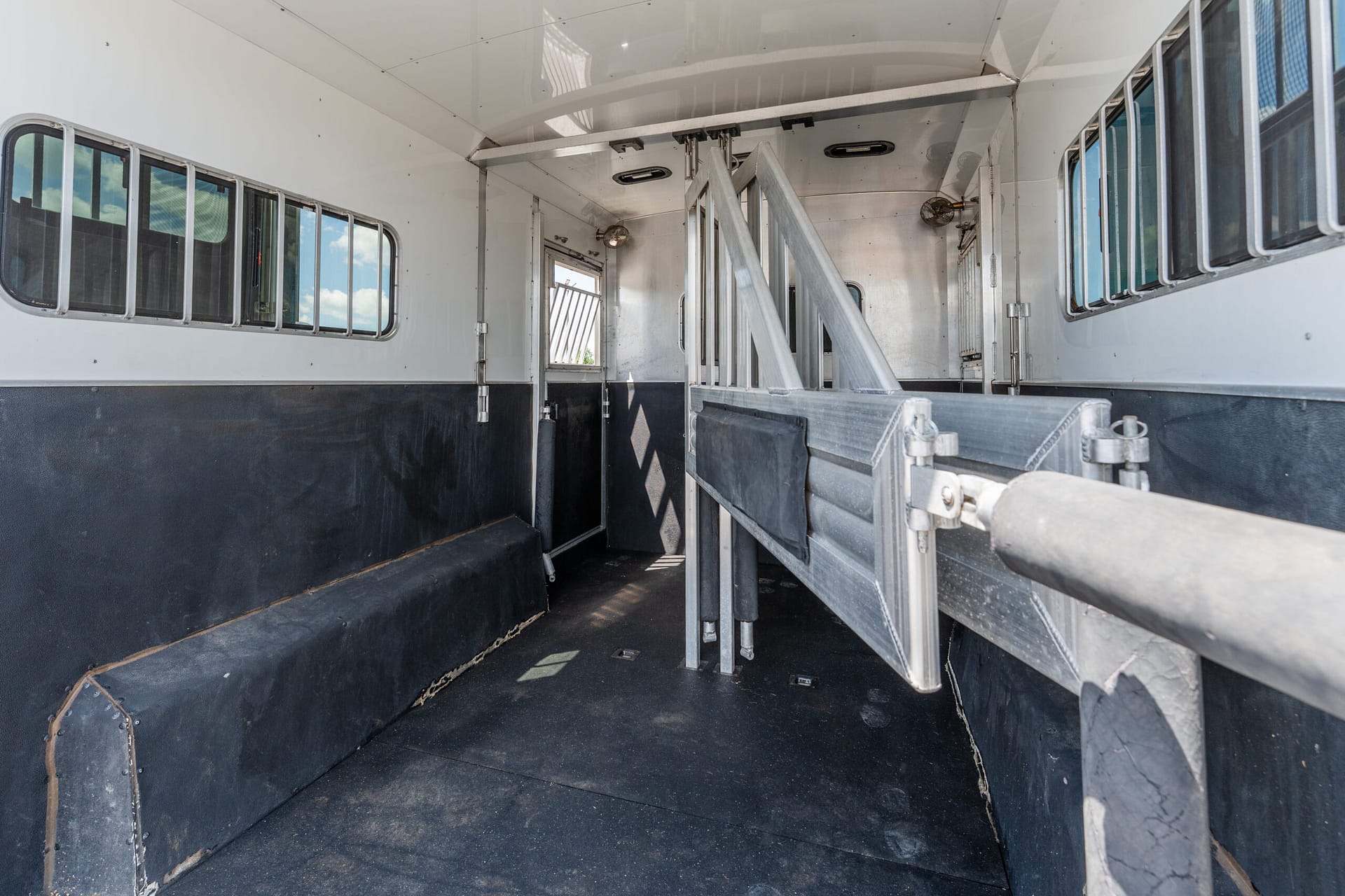 Interior of a metal animal trailer with partition rails and small windows along the sides, dark rubber floor visible.