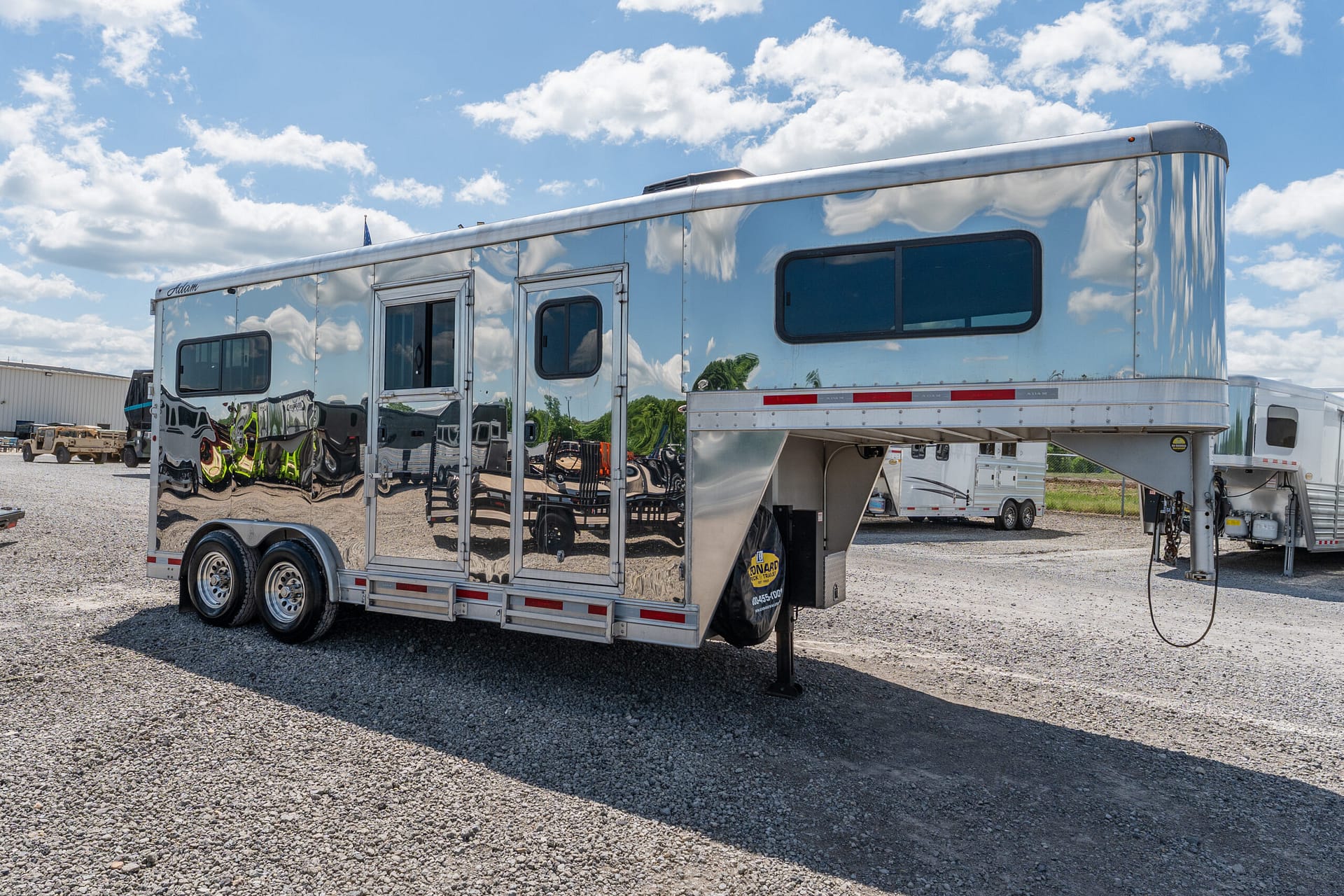 Shiny chrome trailer with rounded front, parked on a gravel lot under a blue sky with clouds.