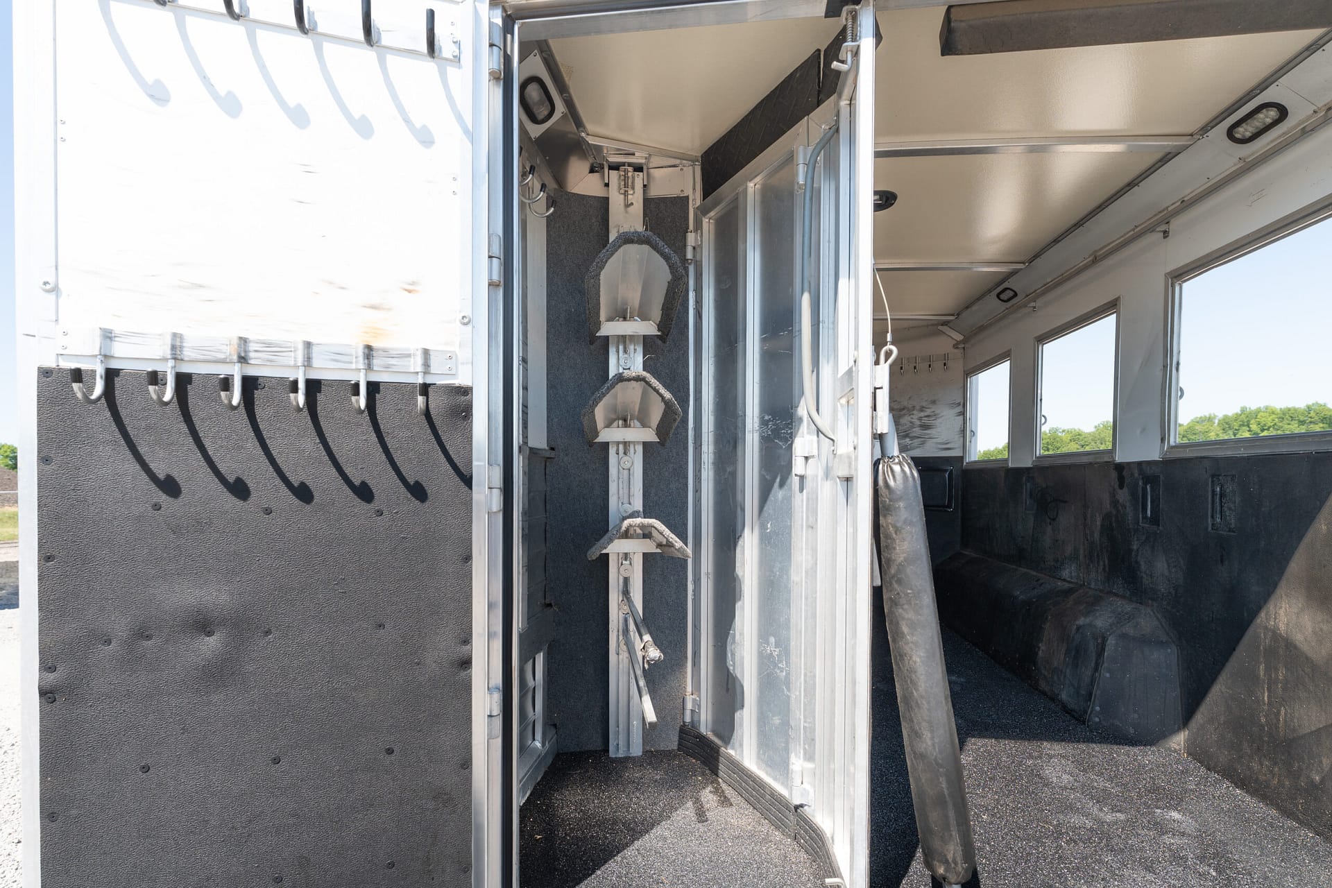 Open horse trailer interior showing a vertical metal stair ladder with foam rungs and hanging hooks along the wall
