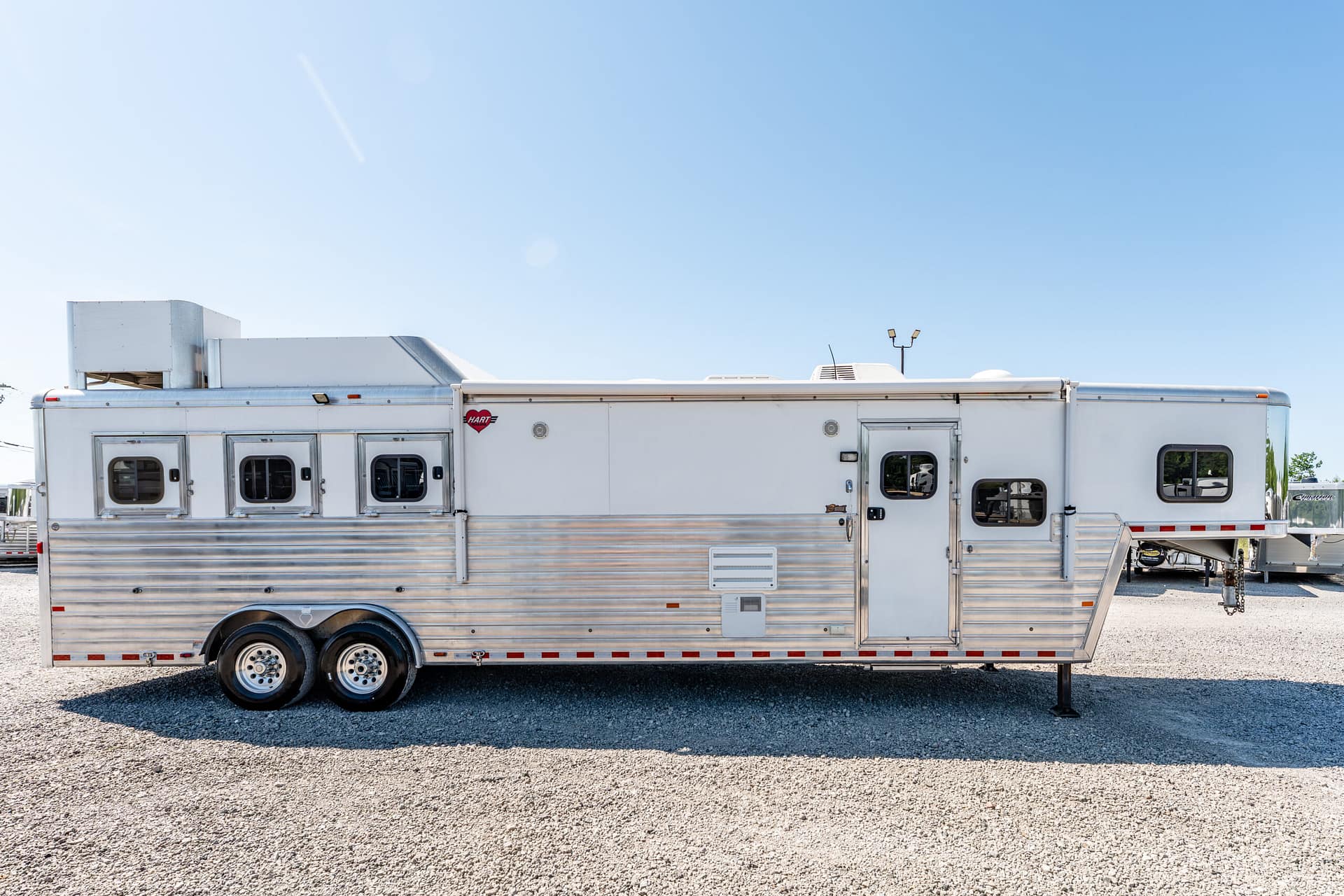 Long silver aluminum trailer parked on a gravel lot under a clear blue sky.