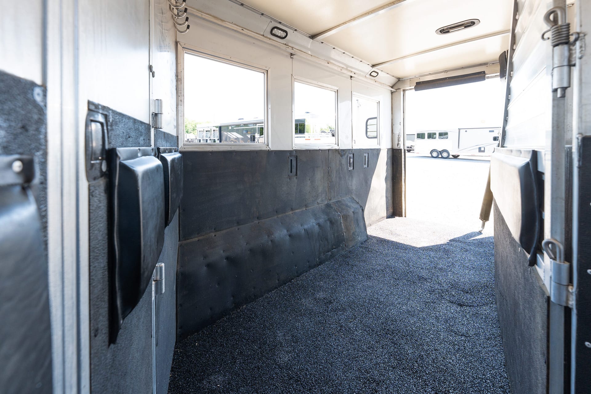 Interior of a white utility trailer with black padded walls and side windows, bright outdoor light visible through the openings.