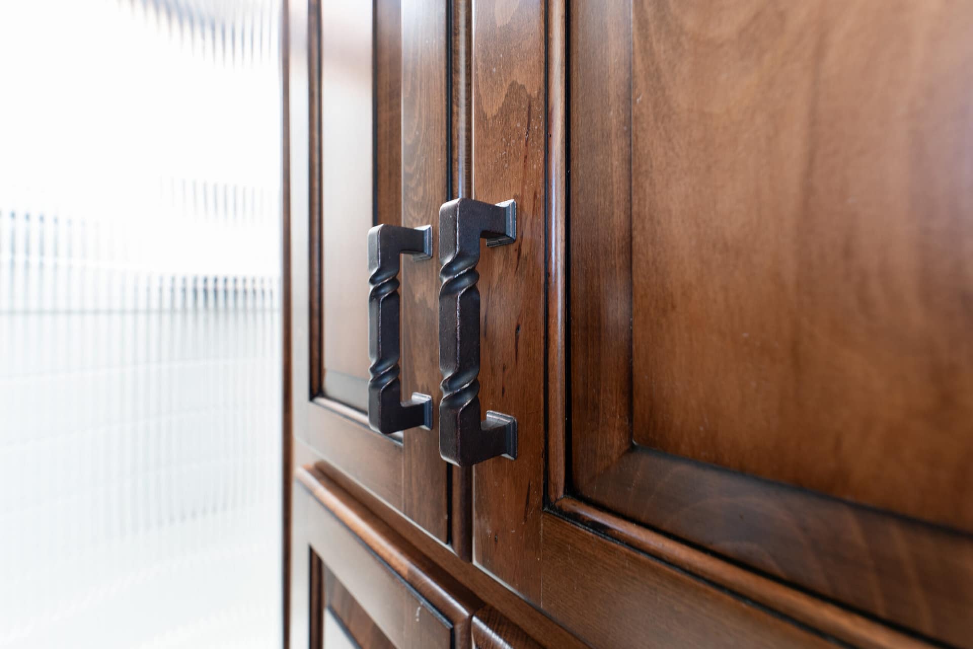Close-up of dark wooden cabinet doors with black twisted-metal handles.