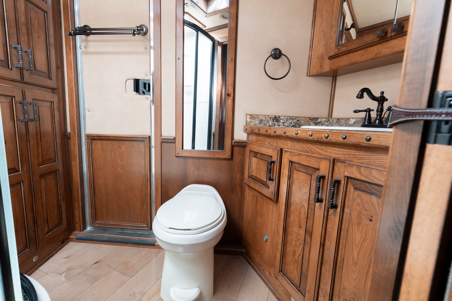Wood-paneled RV bathroom with a white toilet, granite countertop, and mirrored cabinets above the sink.