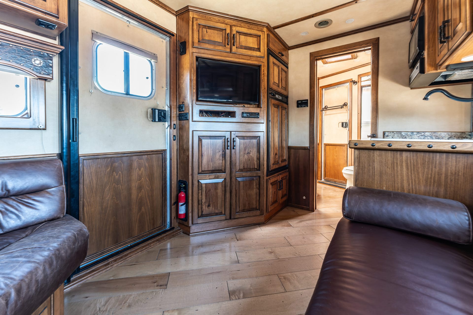 Interior of a wood-paneled RV living area with built-in cabinets and a wall-mounted TV above storage compartments