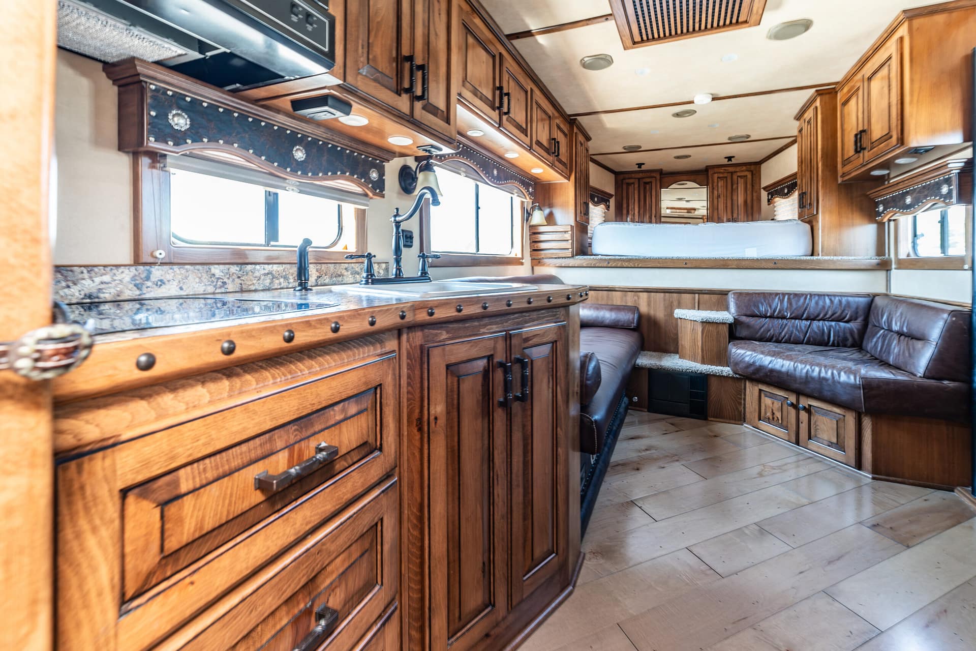 Wood-paneled RV kitchen with granite countertop, black faucet, and built-in appliances; leather sofa visible on the right.