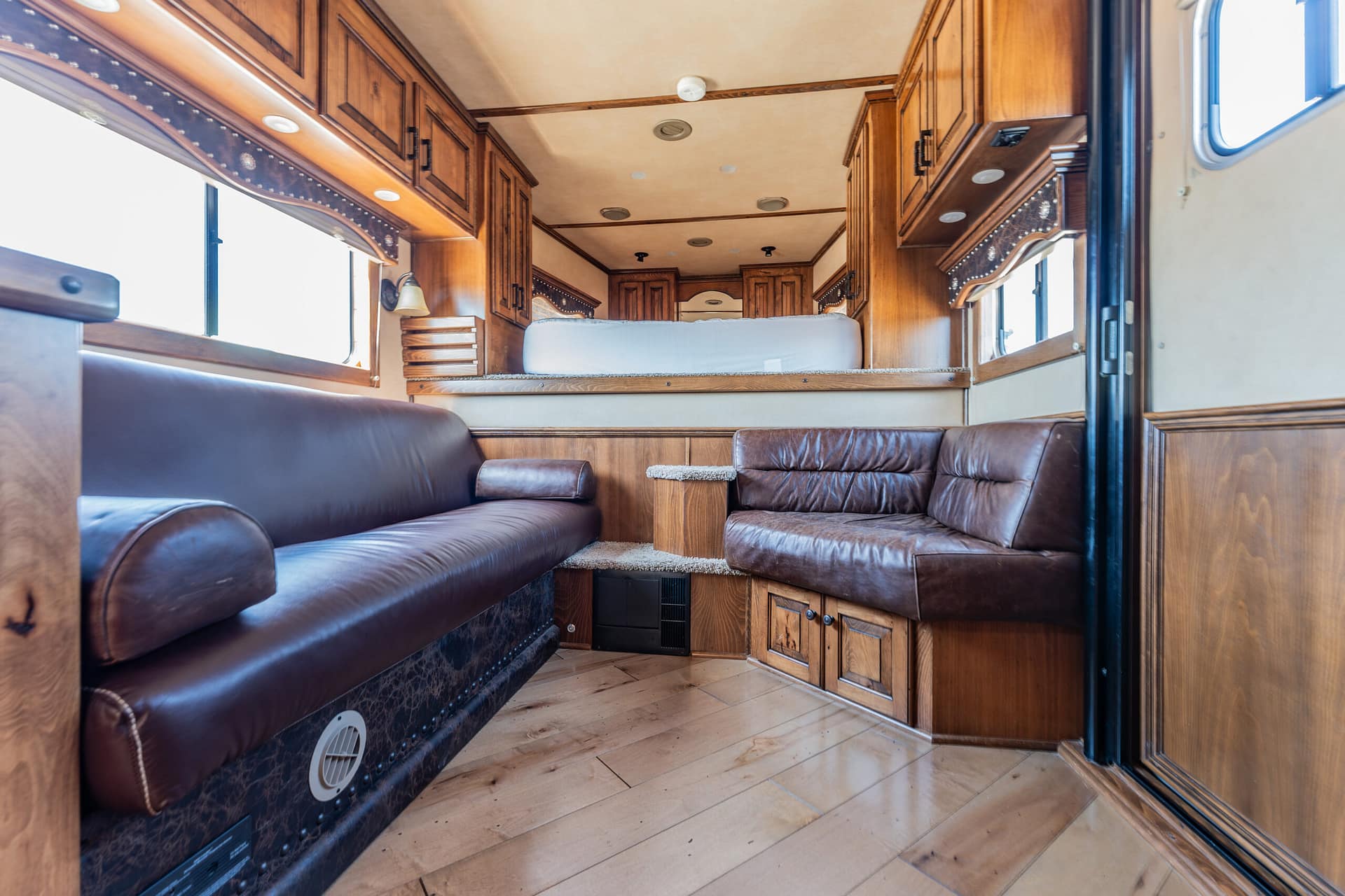 Wood-paneled RV living area with brown leather sofas, built-in cabinets and a bed at the far end.