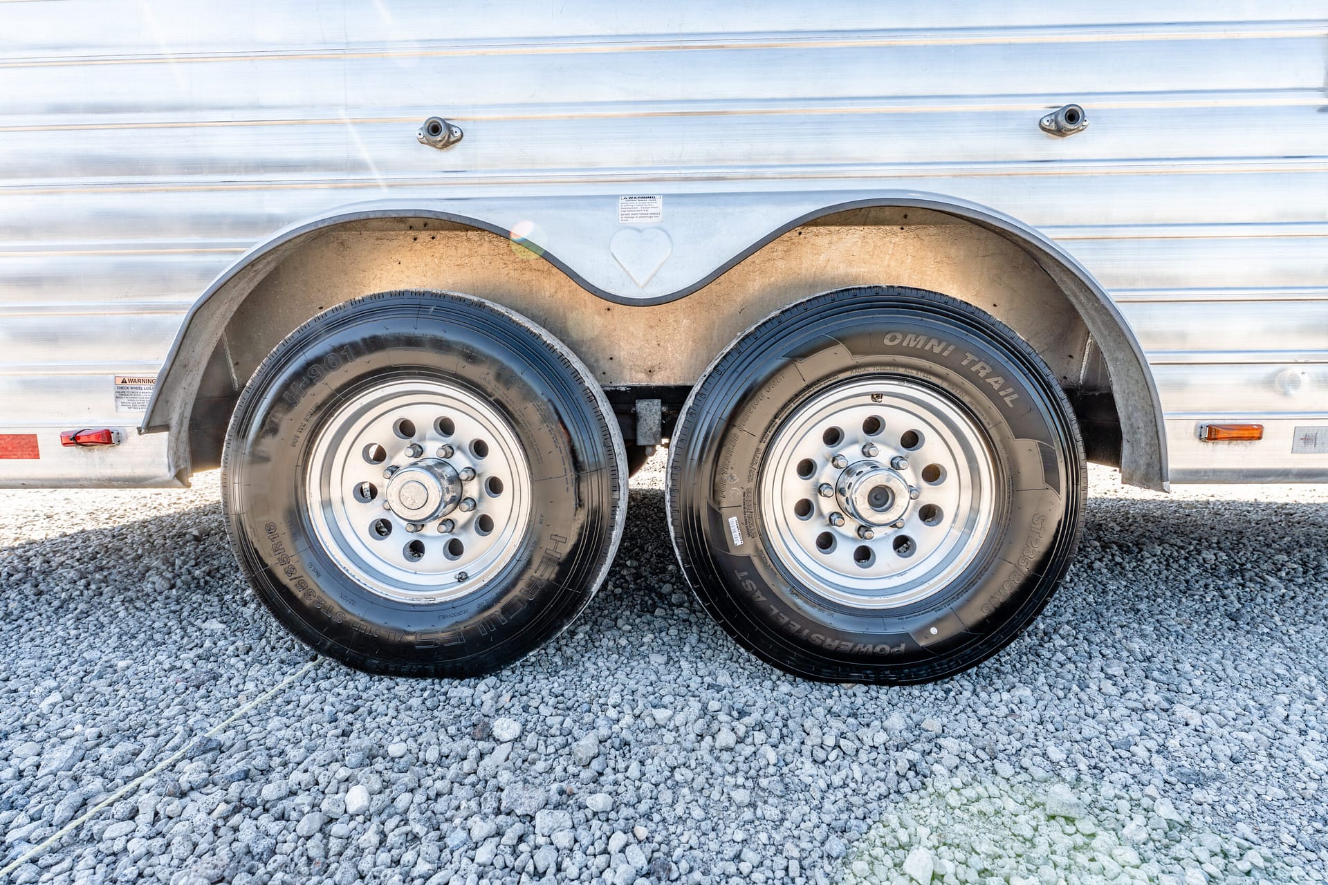 Dual wheels of a silver trailer with curved fenders on a gravel surface.