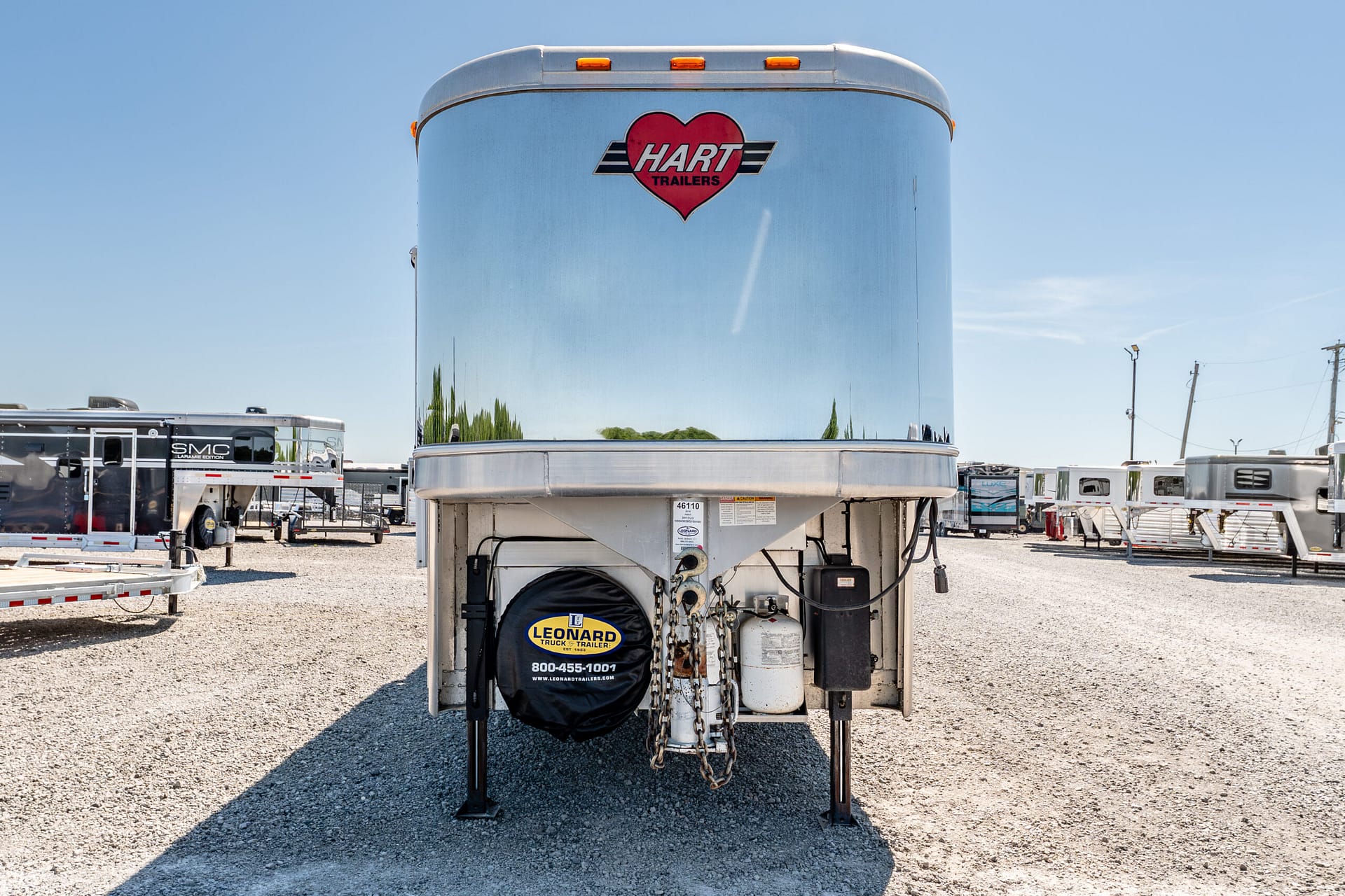 Large blue Hart Trailers trailer in a gravel lot with a red heart logo on the front and orange clearance lights above, under a clear sky