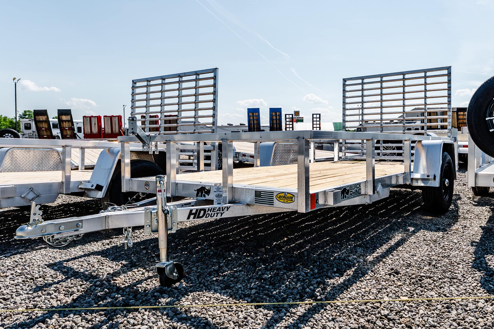 Flatbed trailers with metal rails parked on a gravel lot under a clear blue sky.