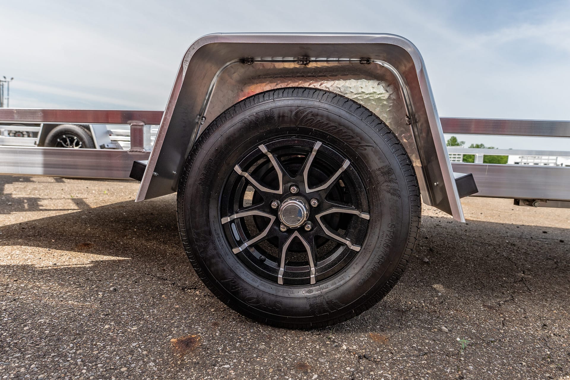 Close-up of a black alloy wheel and tire on a trailer, with a curved metal fender and diamond-plate edge above it.