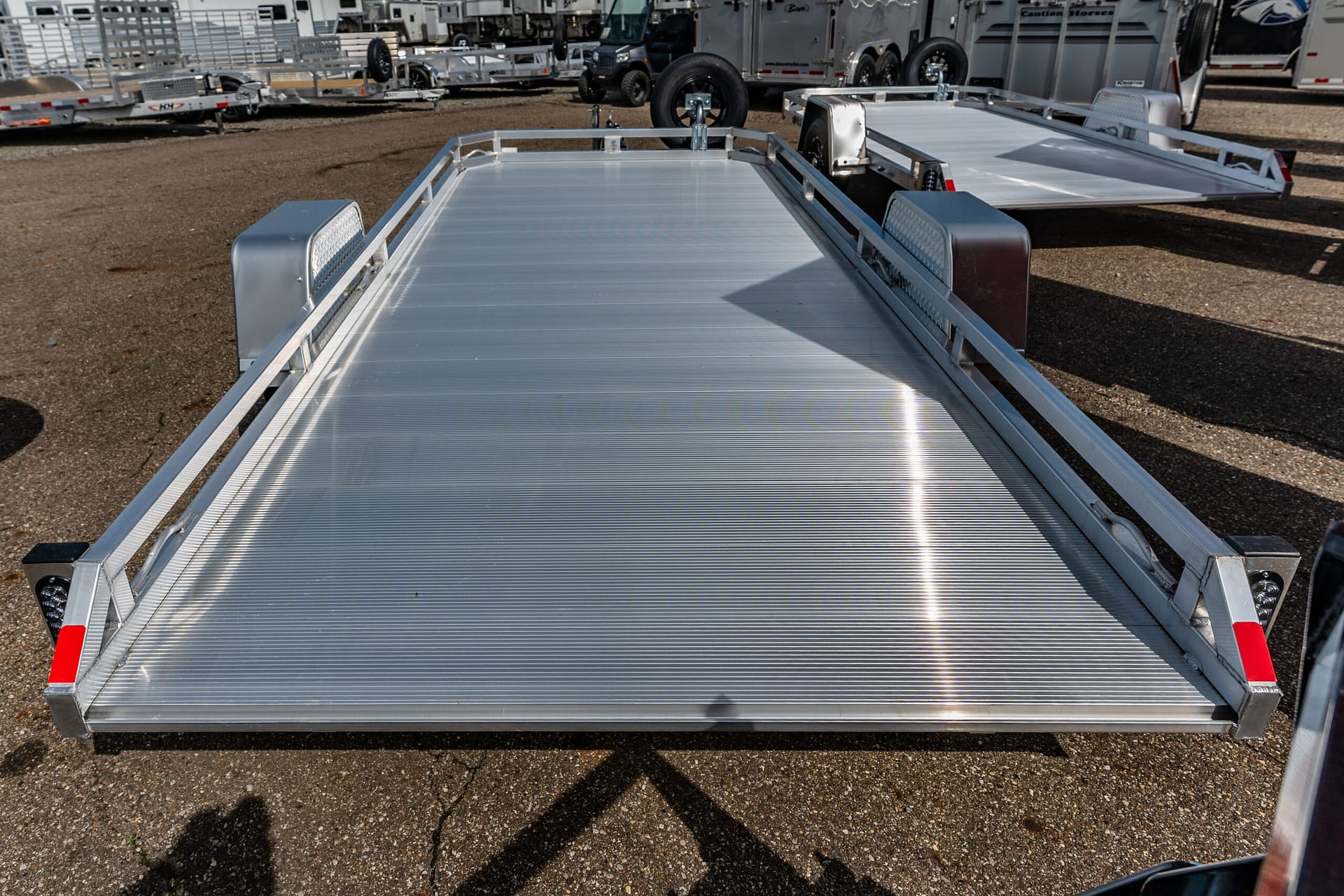 Aluminum flatbed trailer deck with side rails in a yard full of trailers.
