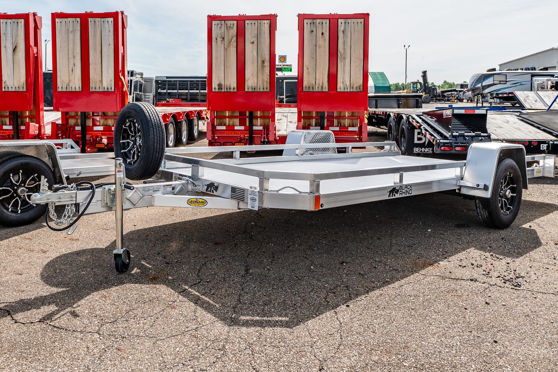 Row of red wooden‑panel trailers on a flatbed trailer in a busy truck equipment yard.