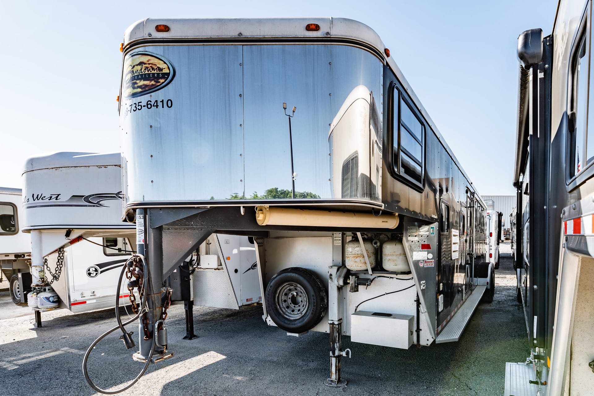 Row of large silver semi-trailers parked side by side in a lot, showing their polished metal exteriors, wheels, and landing gear.