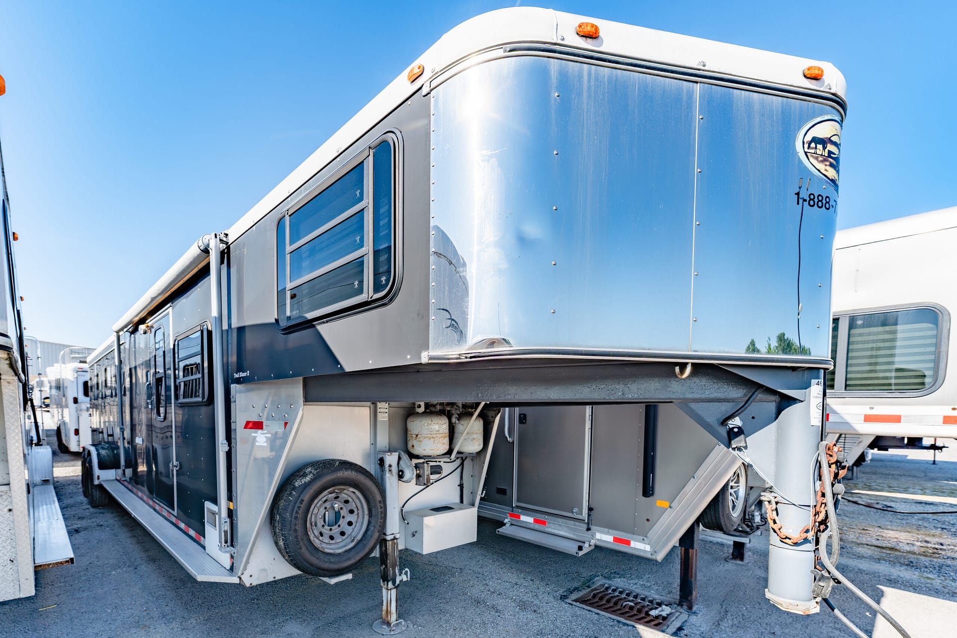 Front corner of a silver travel trailer with elevated front section, jacks on the ground, and orange marker lights against a blue sky