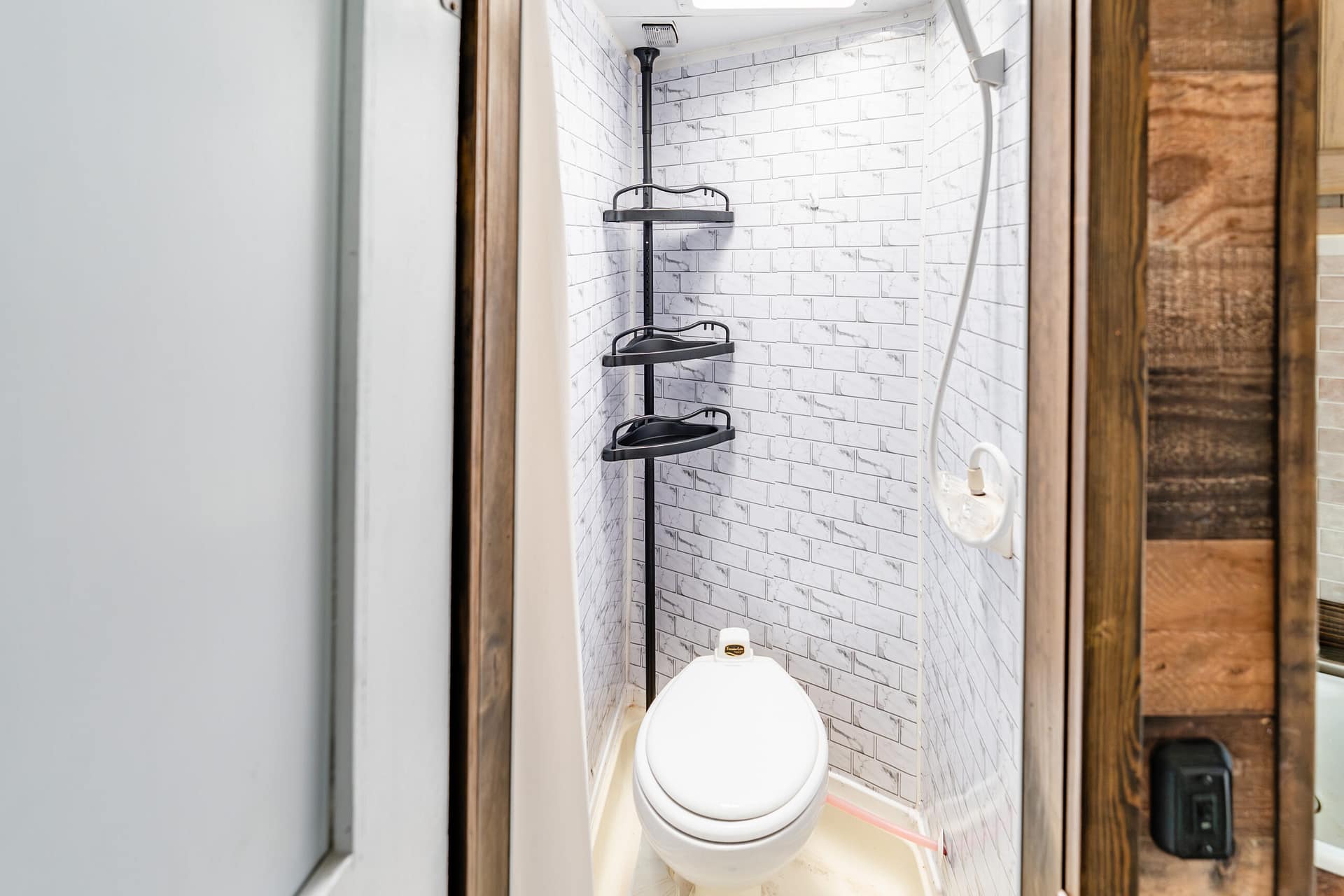 Small bathroom with a white toilet, black metal corner shelves, and white brick-pattern tiles on the walls.