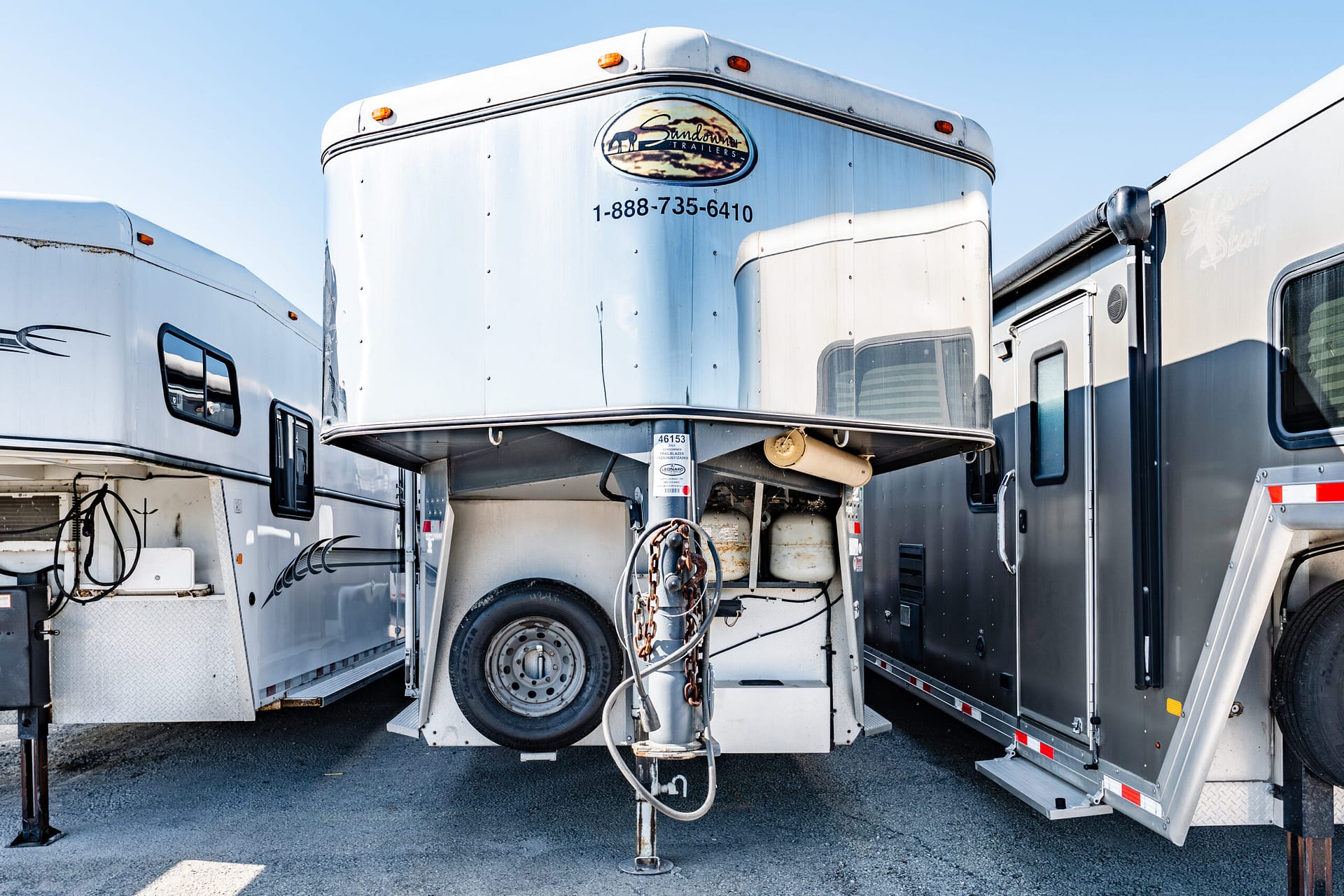 Front view of a silver horse trailer with a hitch, parked among white and gray trailers in a lot.