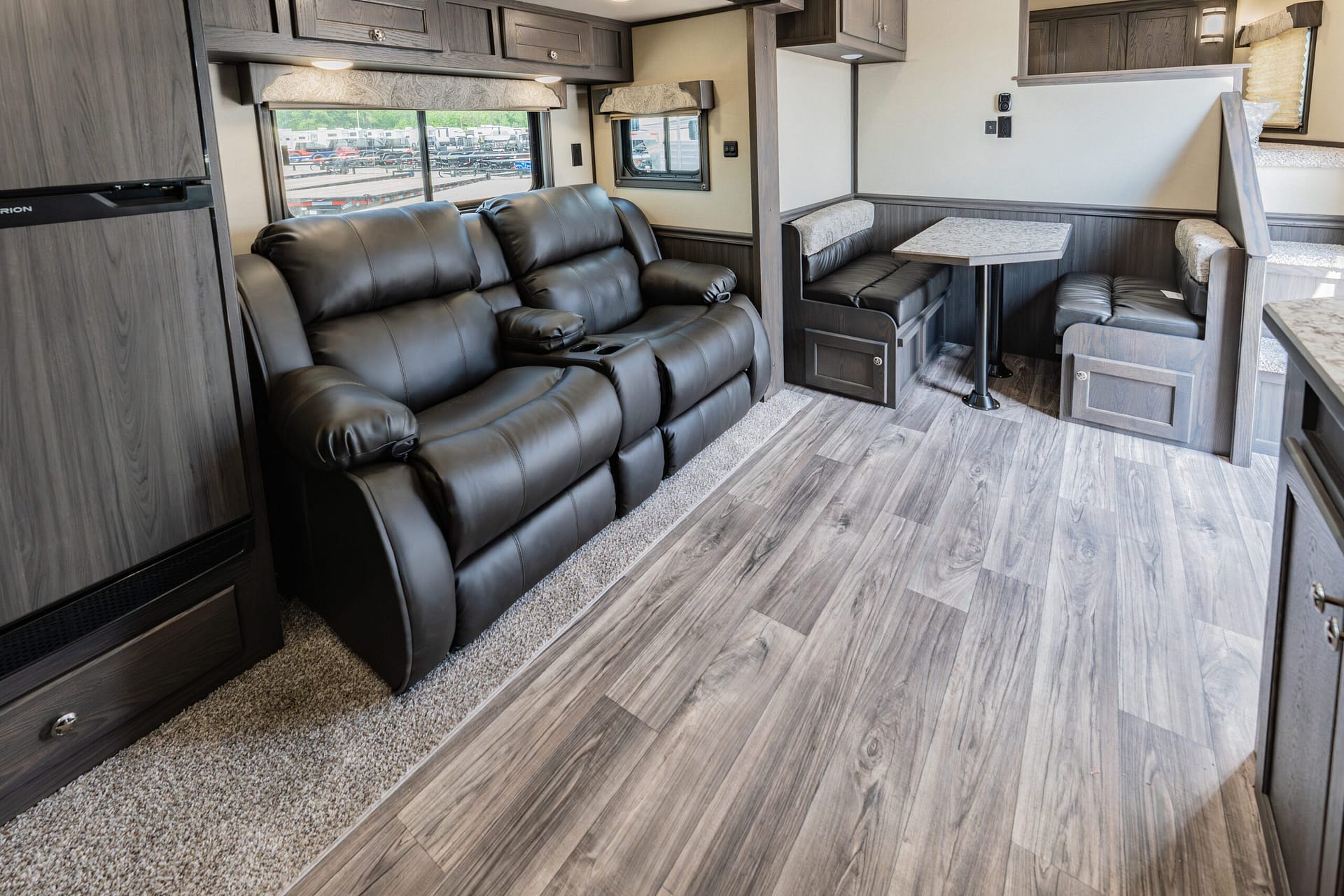 Cozy RV living area with a black leather reclining sofa, booth dinette, and built-in cabinets above.