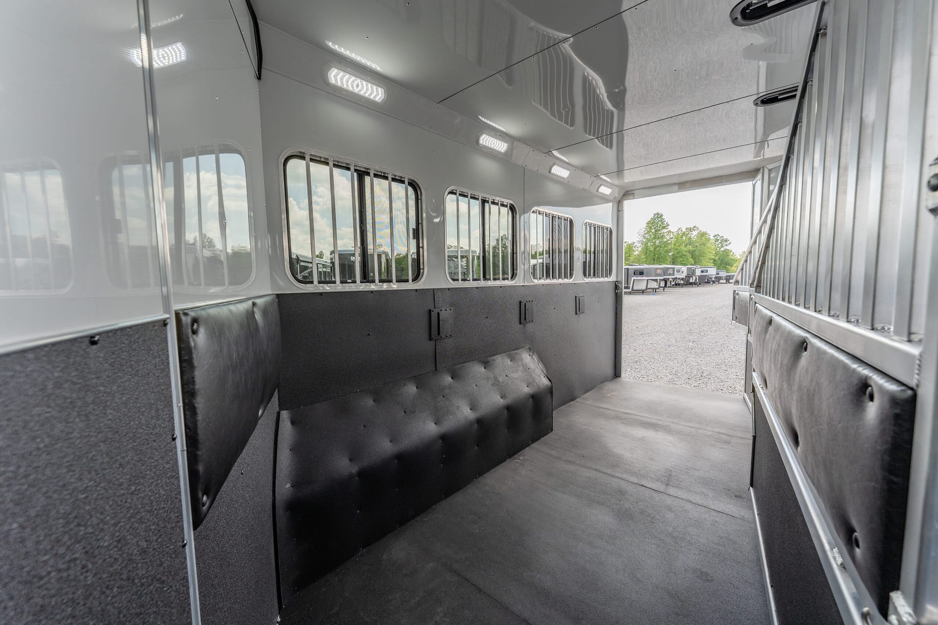 Interior of a silver horse trailer with a black padded divider and barred windows along the sides, empty and ready for use