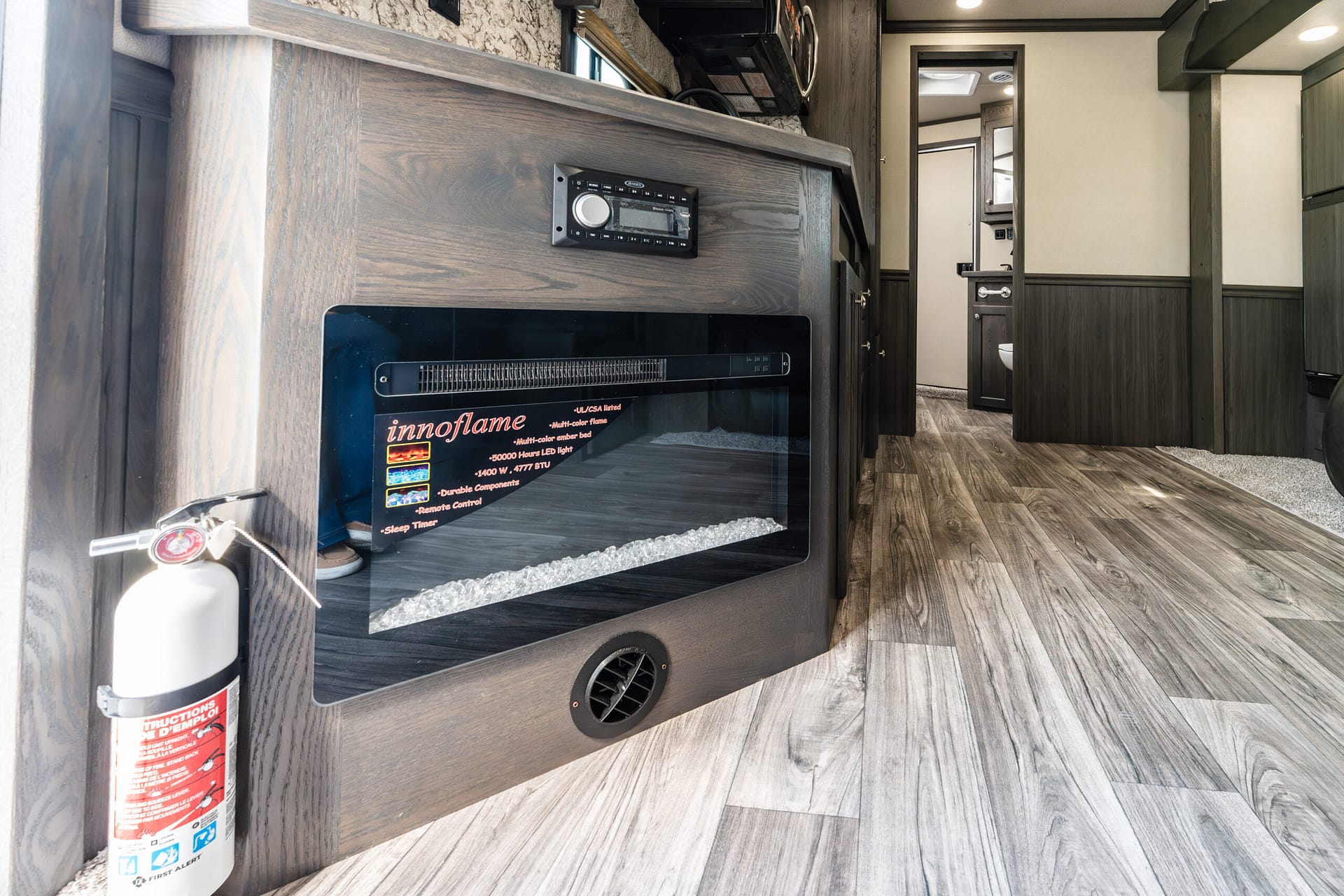 Interior of a camper/RV living area with a built-in fireplace labeled 'innoflame' and a wall-mounted control panel nearby, plus a fire extinguisher at left coast.