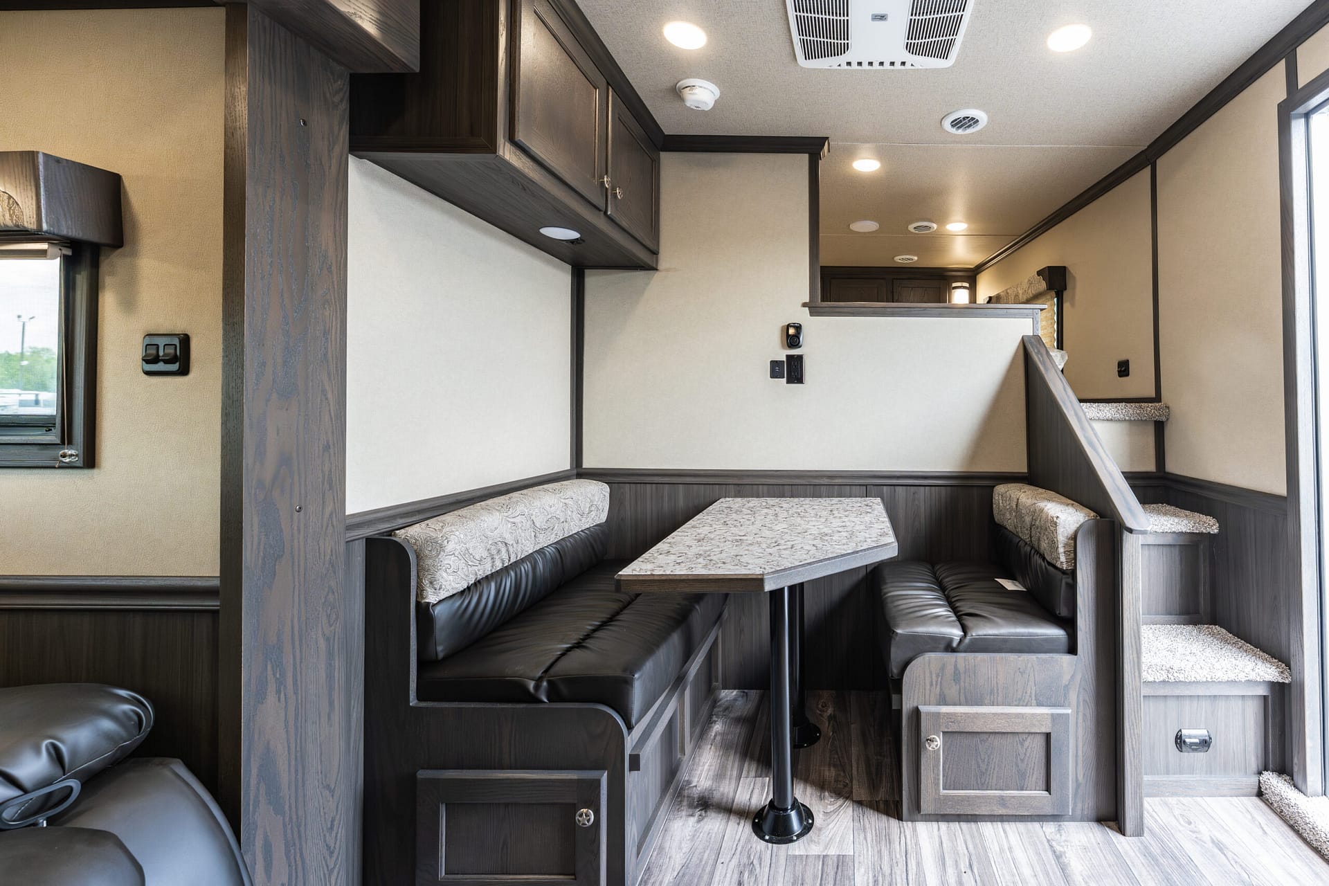 RV dining booth with dark wood seating, beige walls, and a marble-pattern table under overhead cabinets