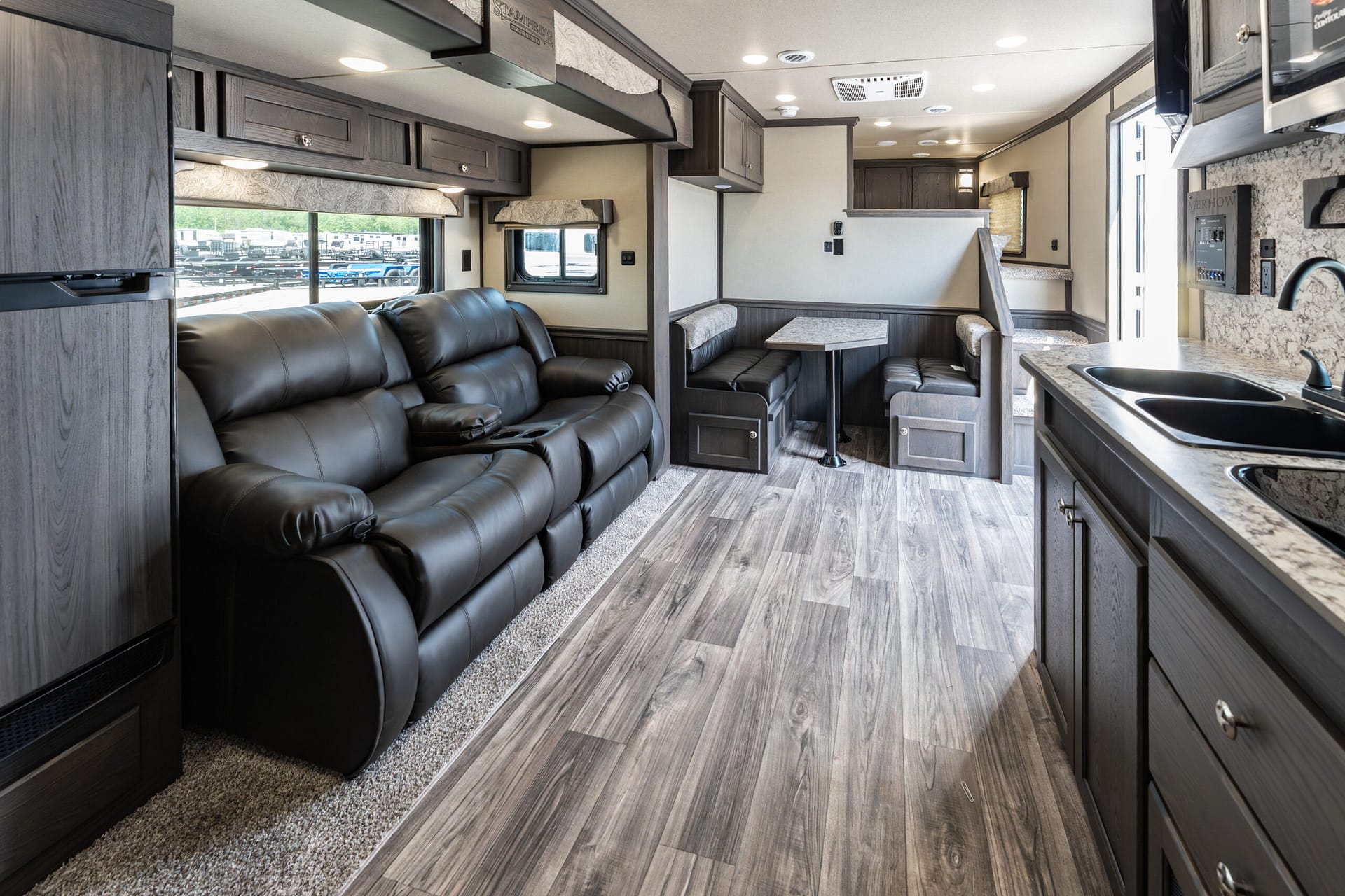 Interior view of a modern RV living area with a black leather sofa, dinette, and kitchenette