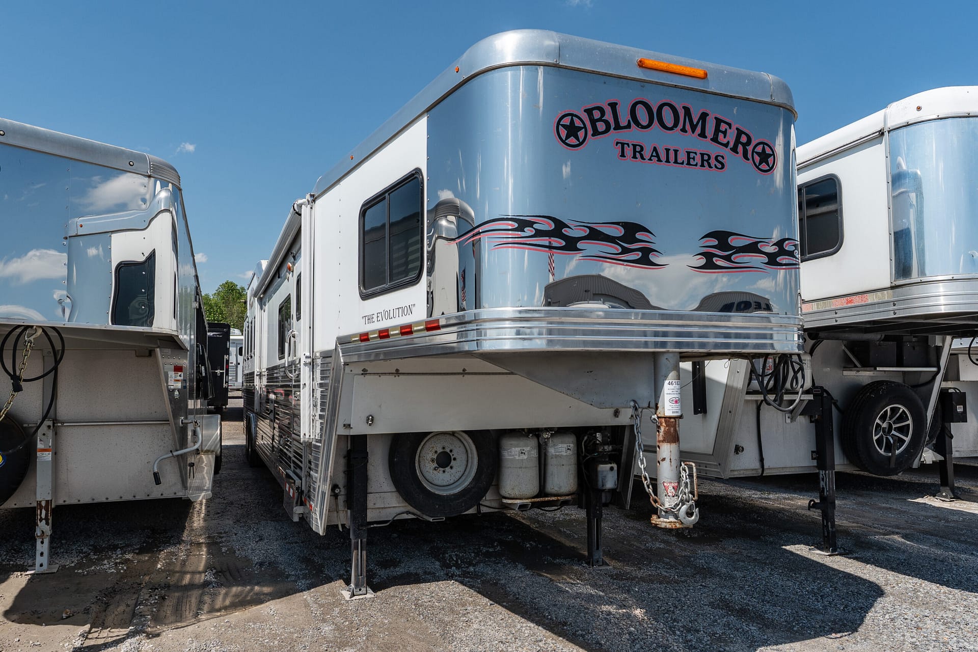Silver Bloomer Trailers semi-trailer with black-and-red flame graphics, parked in a lot under a blue sky.