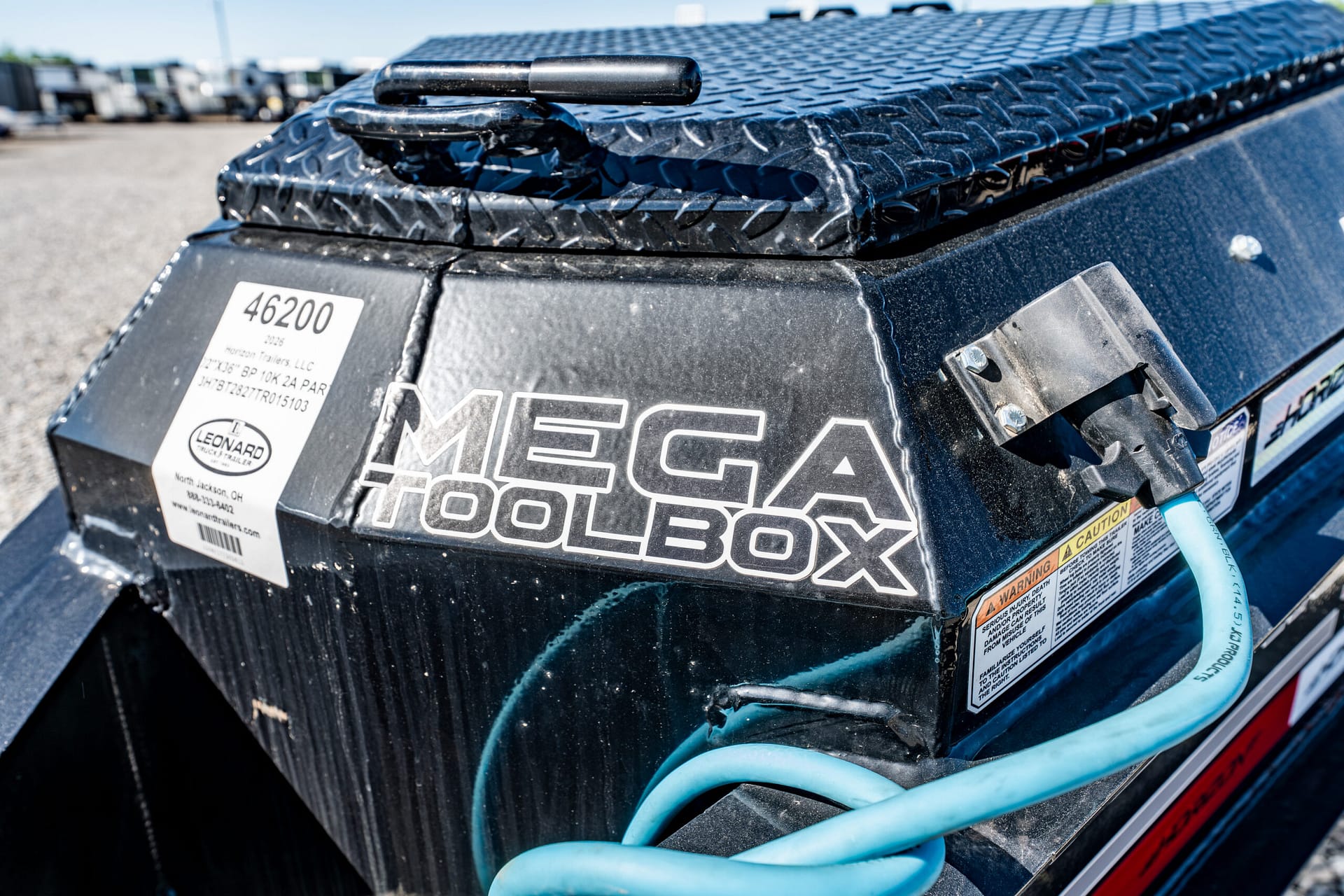 Close-up of a black diamond-plate truck toolbox with a latch, showing the large 'MEGA TOOLBOX' branding and blue hoses nearby.