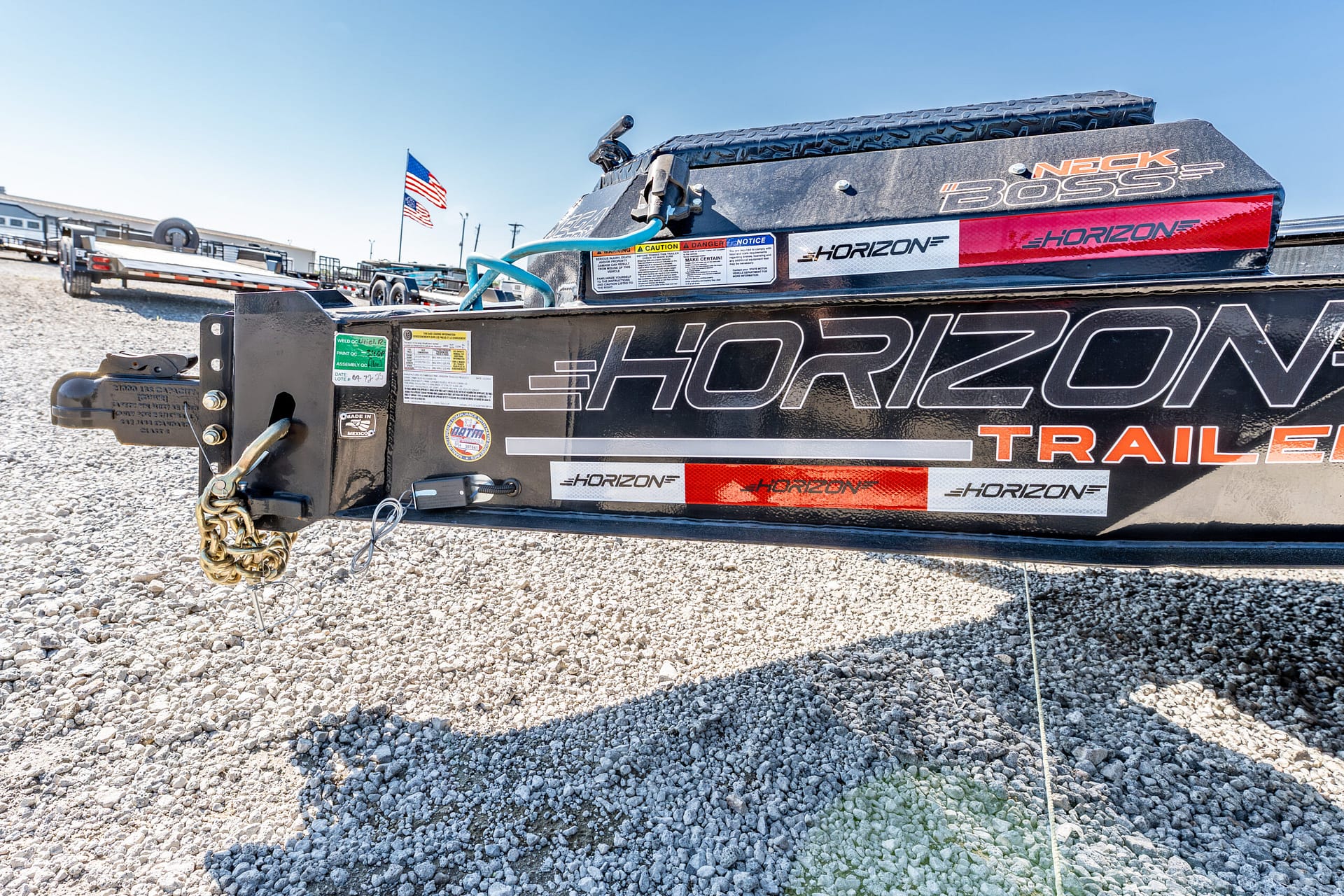 Close-up of a Horizon trailer hitch on a gravel lot, with safety chains and a flag in the background.”,