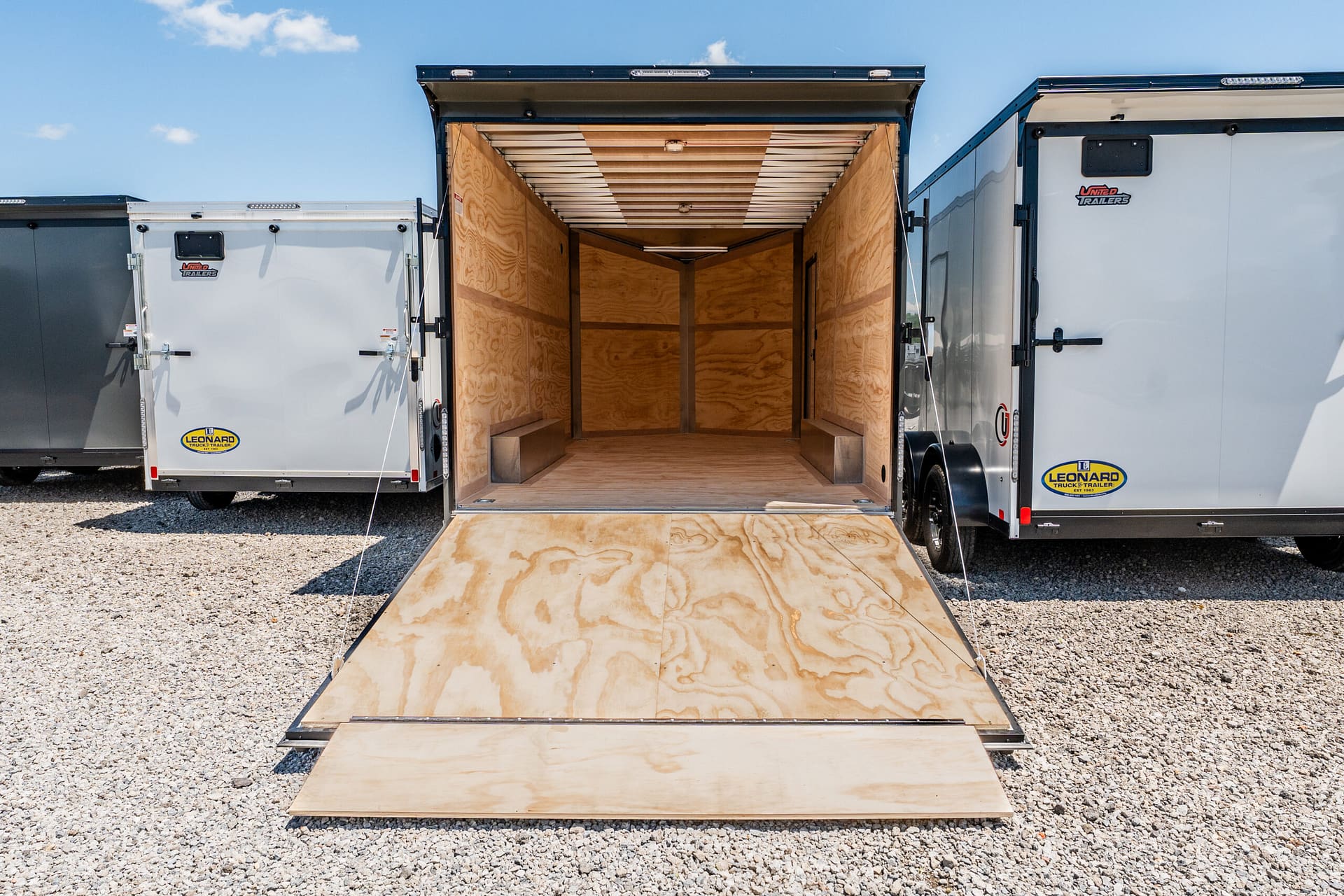 Open trailer with ramp lowered, showing empty wooden interior ready for loading on a gravel lot