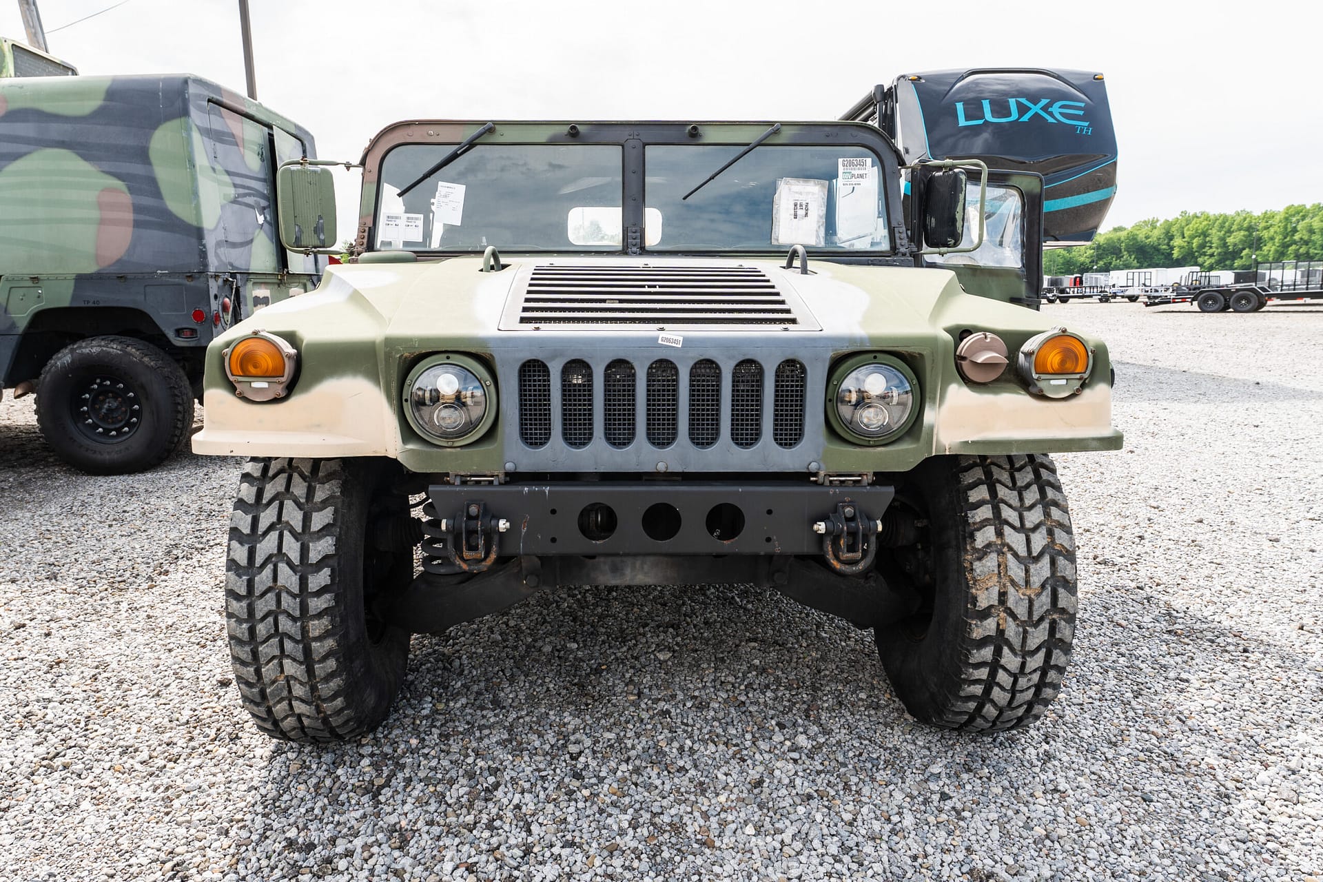 Front view of a desert camo military jeep with large off-road tires on a gravel lot, facing the camera.