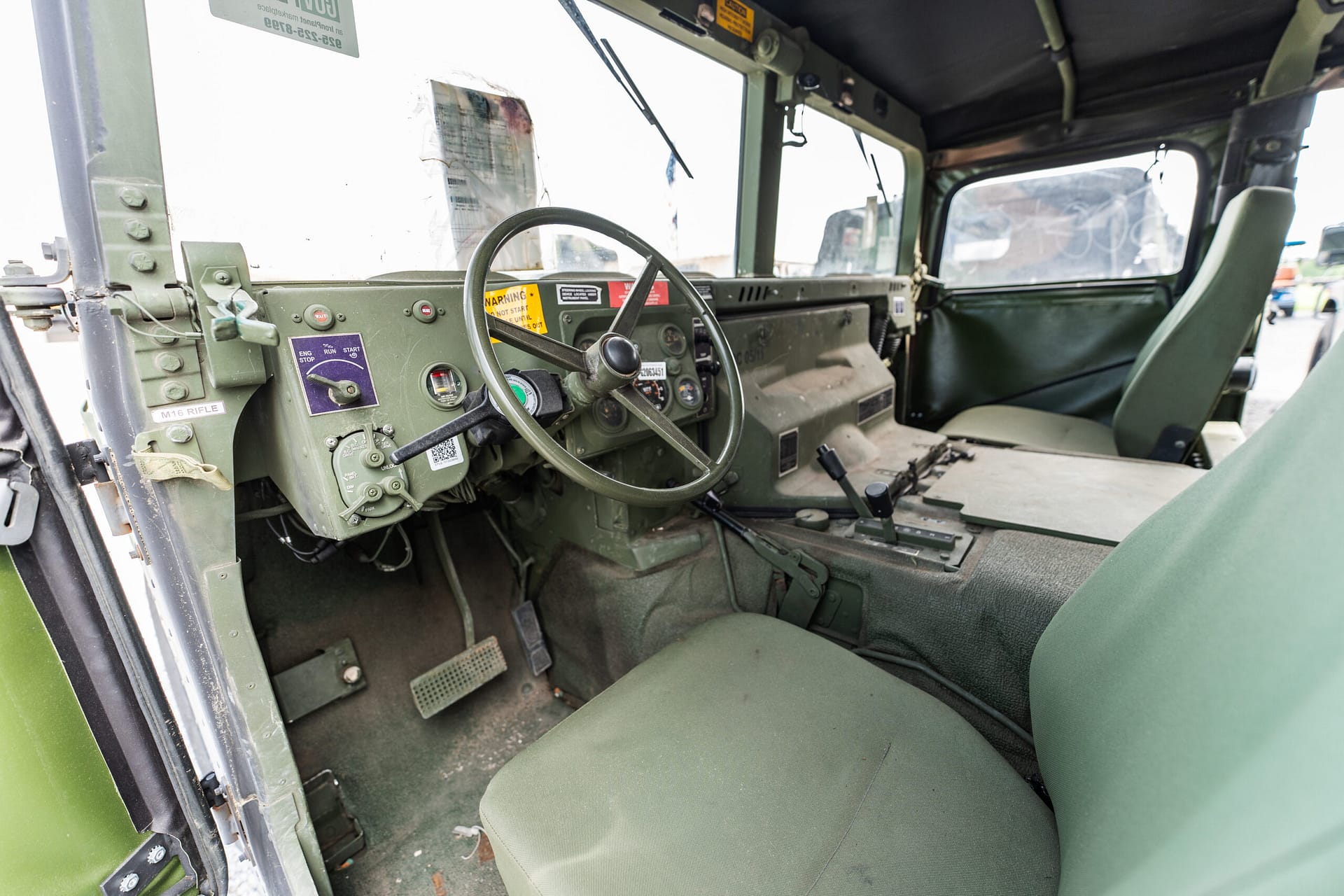 Interior of a military jeep cockpit with green dashboard, steering wheel, and front seats