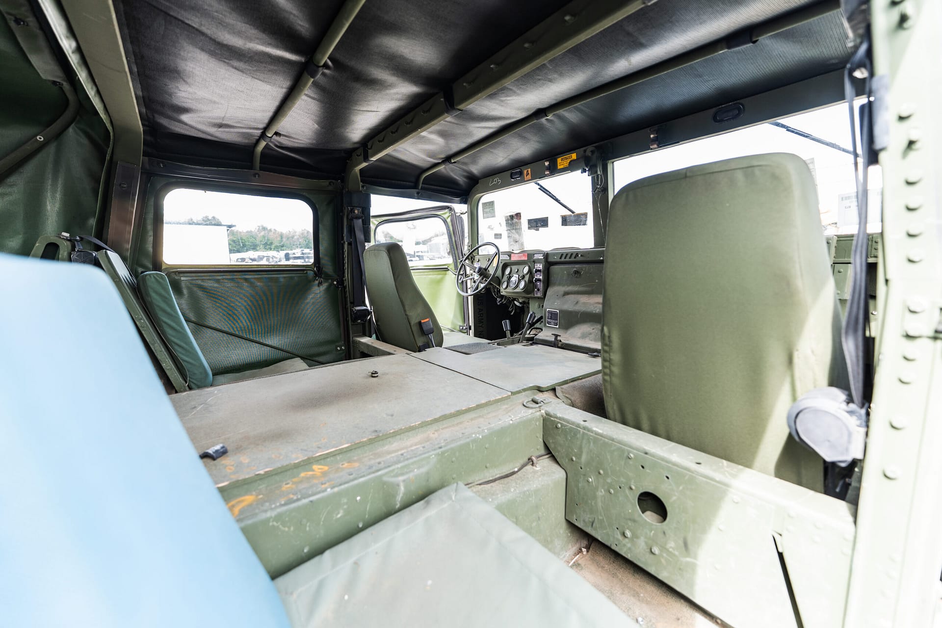 Interior of a military transport aircraft showing green seats, metal framework, and an open cargo area.