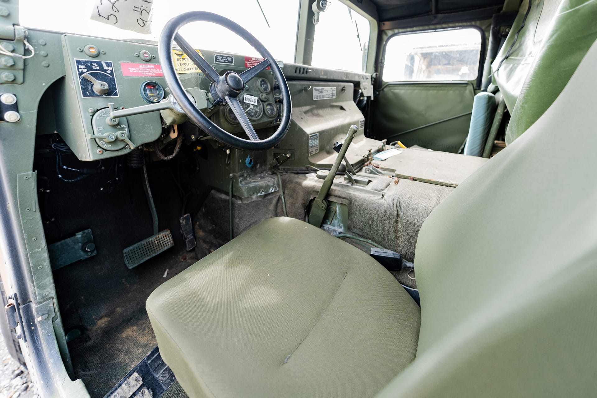 Interior of a vintage military jeep showing a green dashboard with a large steering wheel and worn seats.