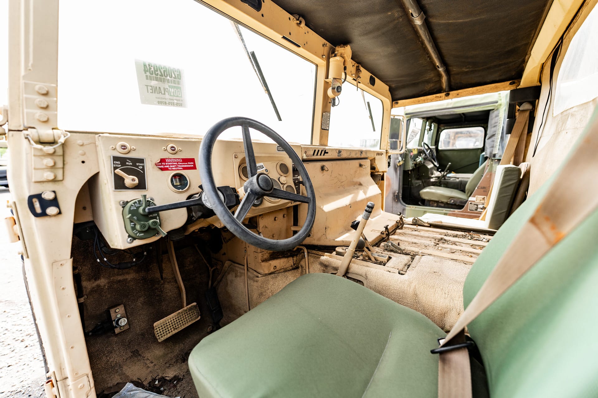 Interior of a dusty, beige utility vehicle cab with steering wheel and dashboard controls visible