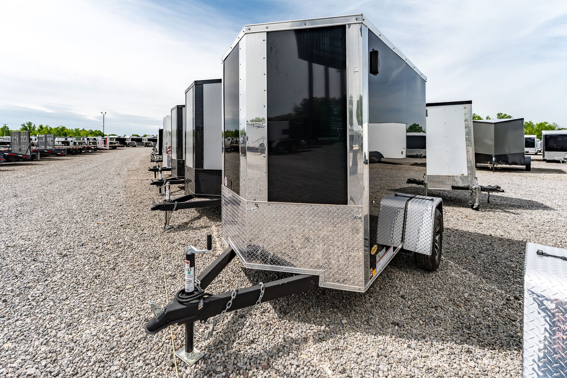 Row of enclosed cargo trailers on a gravel lot, with a large black-and-silver trailer in the foreground.