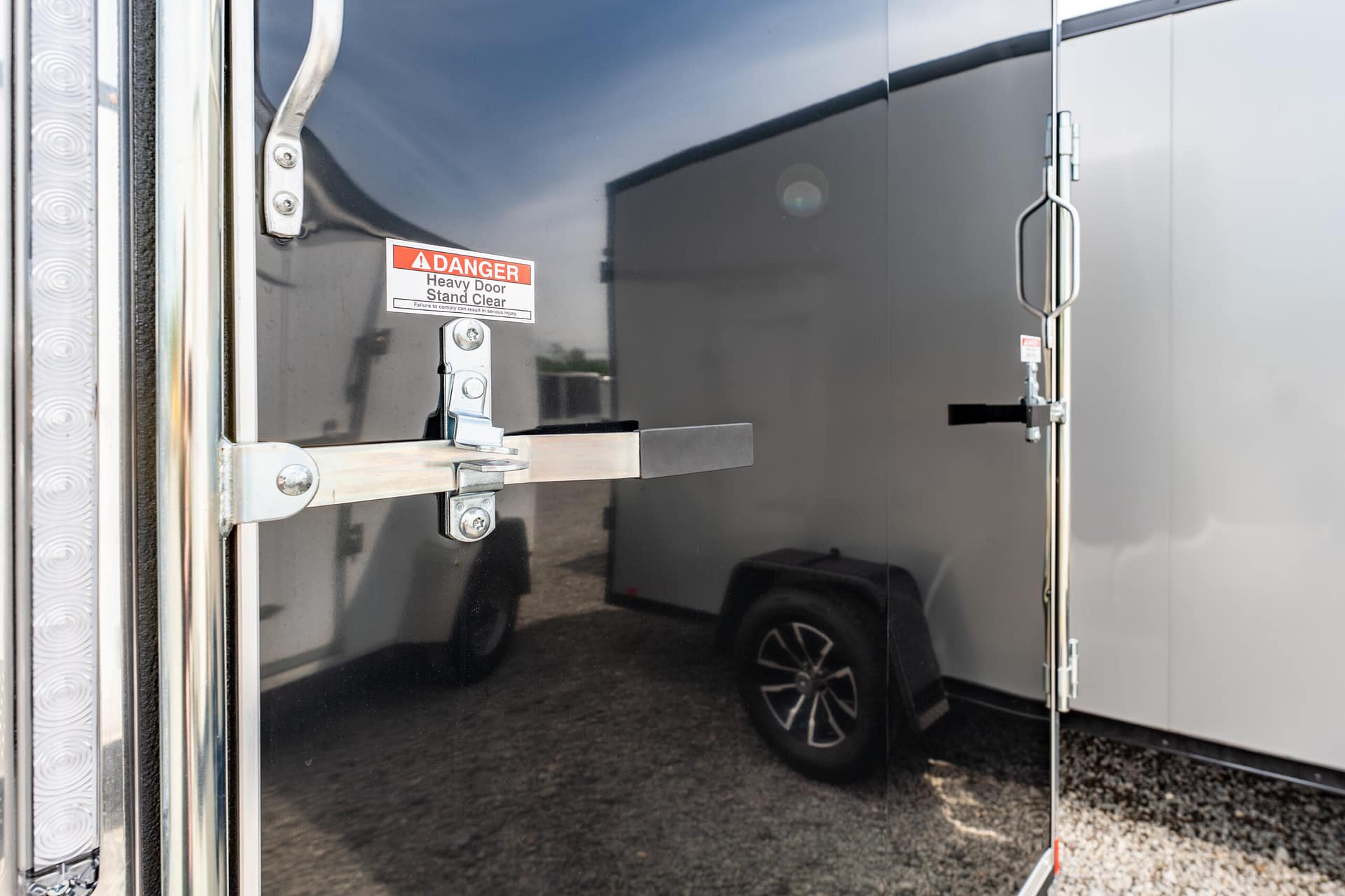 Close-up of a dark trailer door with a 'DANGER Heavy Door Stand Clear' warning label and metal latches.